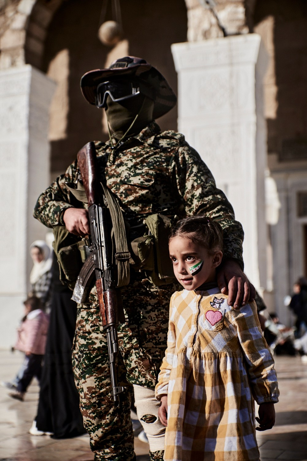 Damas, 16 décembre 2024 – Une fillette pose en compagnie d'un rebelle ayant participé à l'offensive conduisant à la chute de Bachar al-Assad, dans la cour de la Mosquée des Omeyyades, pour une photo historique.