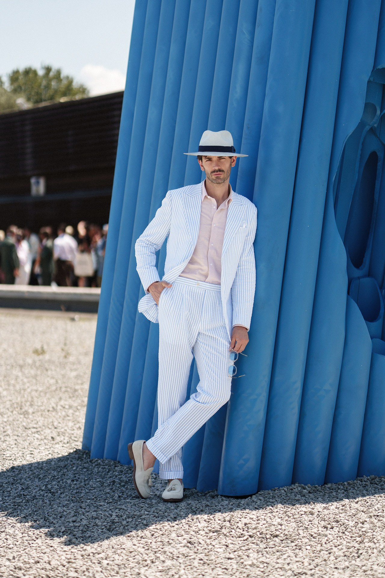 Ospite di Pitti Uomo 110 in completo azzurro a righe in posa accanto all’installazione blu