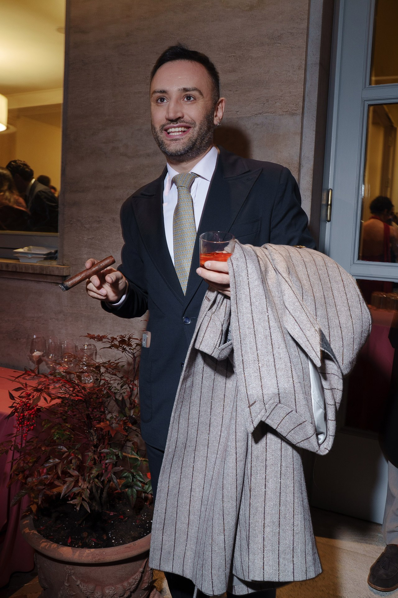 Guest in black suit holding cocktail and coat at evening private event