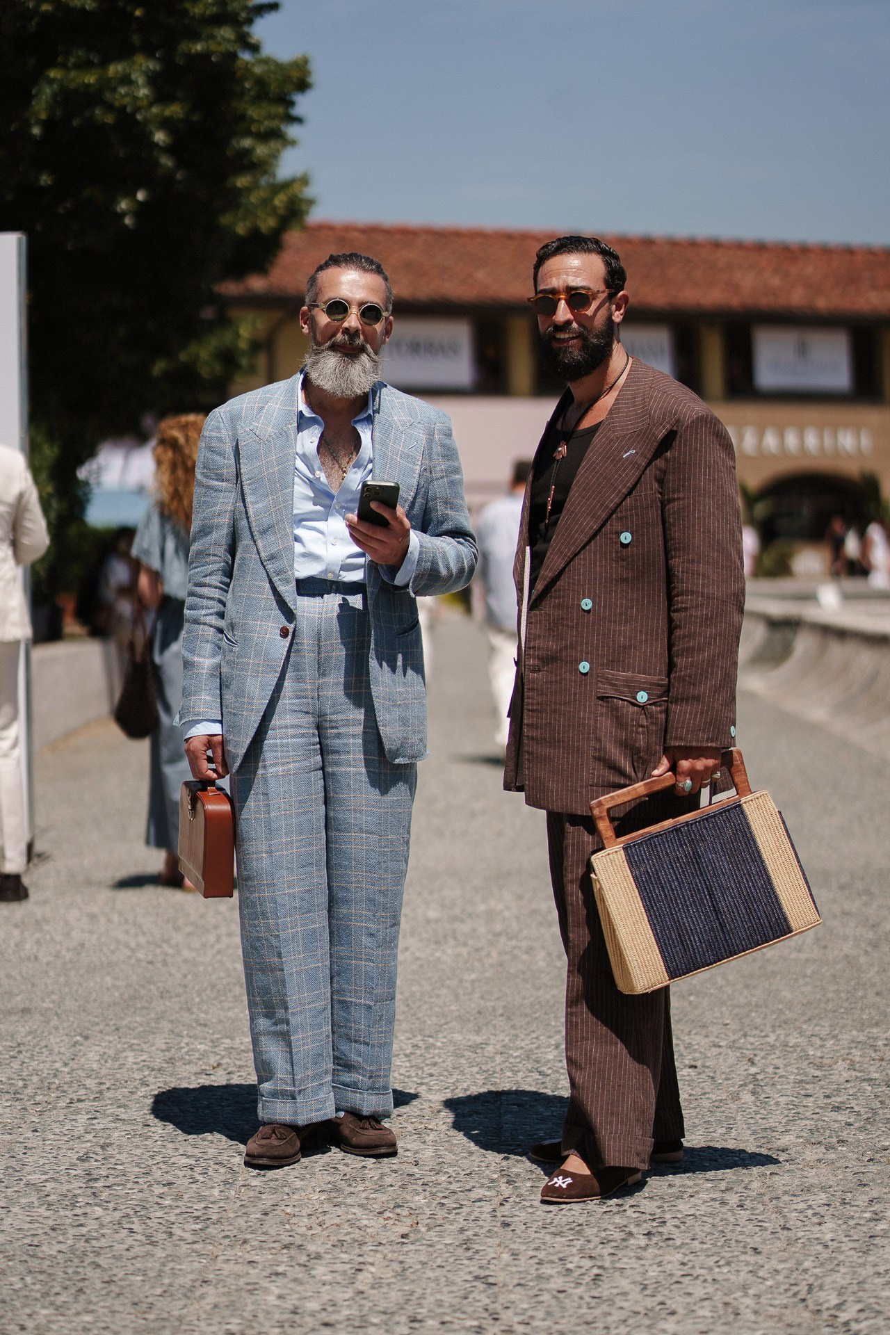 Ritratto street style da Pitti Uomo 110, due ospiti in completi sartoriali blu e marrone con borse in pelle
