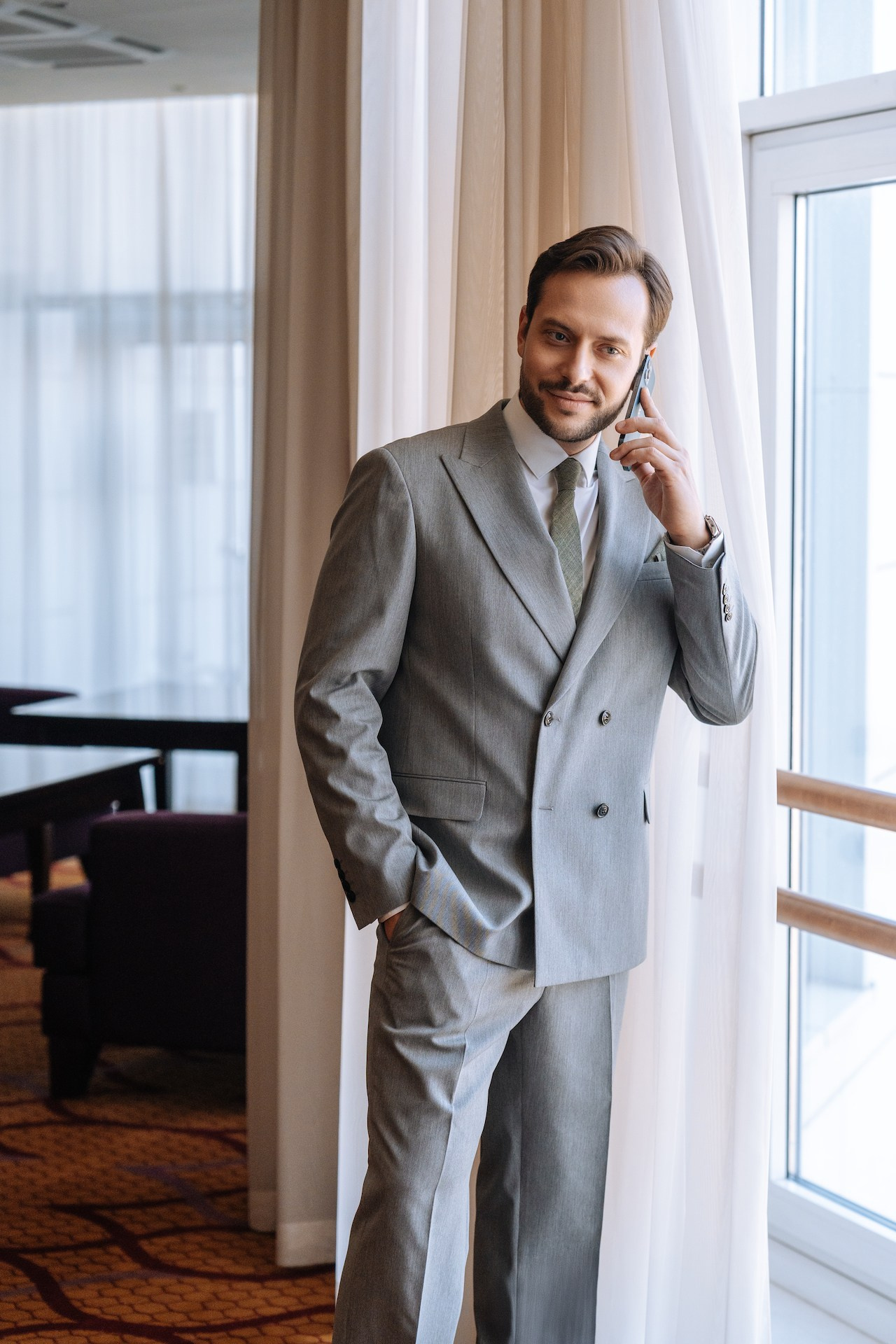 Мужчина разговаривает по телефону у окна в отеле