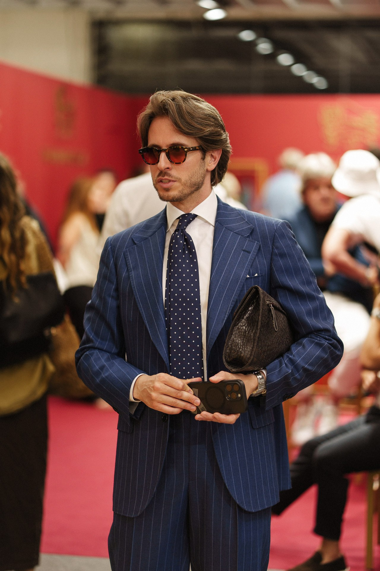 Ritratto menswear da Pitti Uomo 110, ospite in completo gessato blu navy con cravatta e clutch in pelle