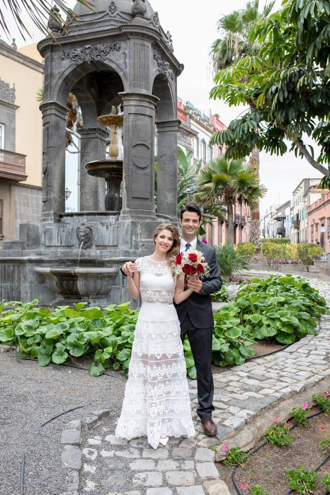 Une mariée et un marié posent devant une fontaine.
