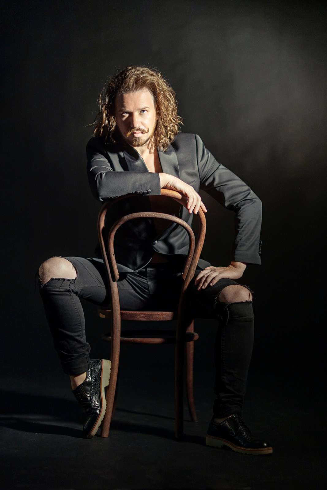Арт-портрет мужчины в чёрной одежде на деревянном стуле, съёмка в студии