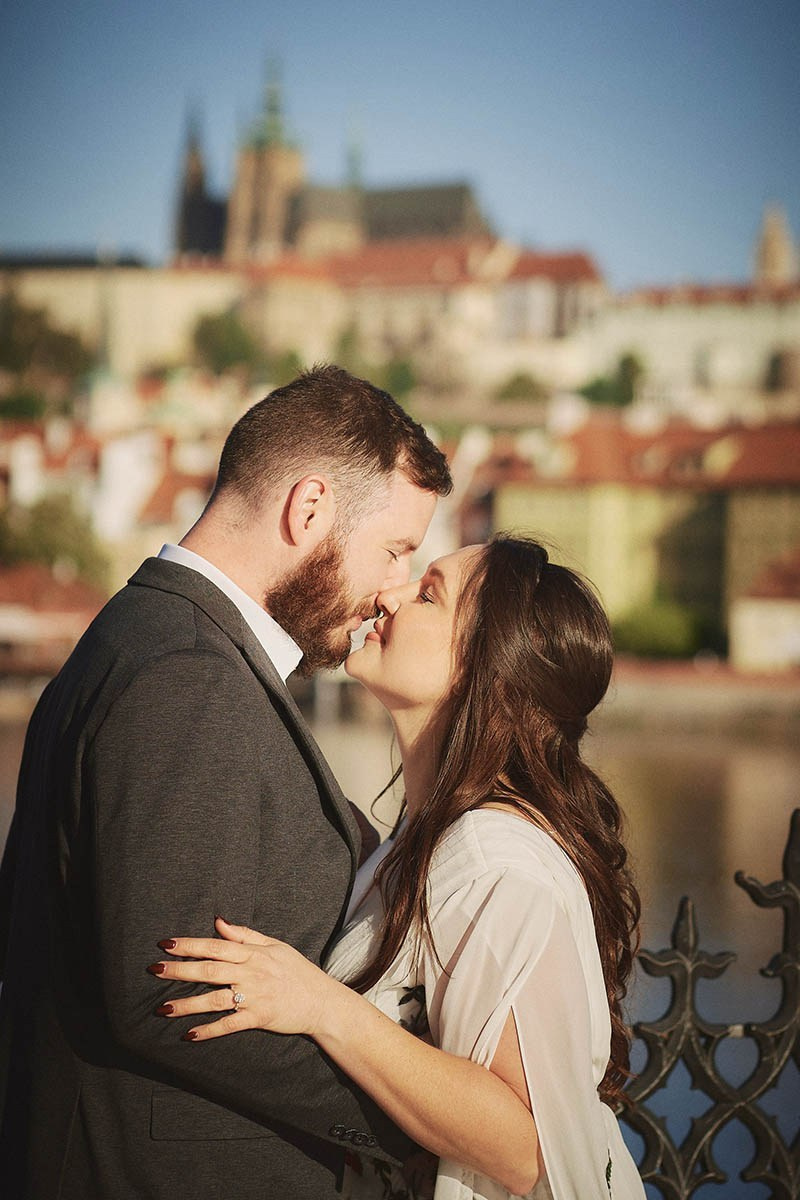 A couple embraces near the riverside as St. Vitus looms behind them in Prague.