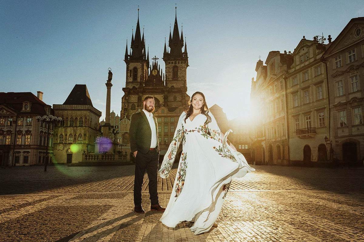 A young American couple bathed in early morning sunlight in the Old Town Square in Prague.