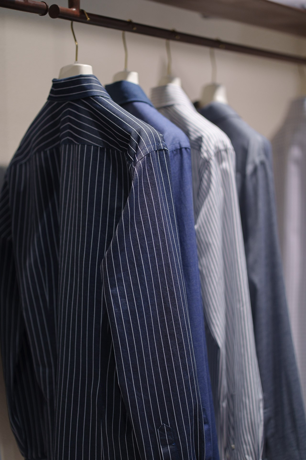 A collection of classic blue and navy striped dress shirts hanging in a luxury boutique setting.