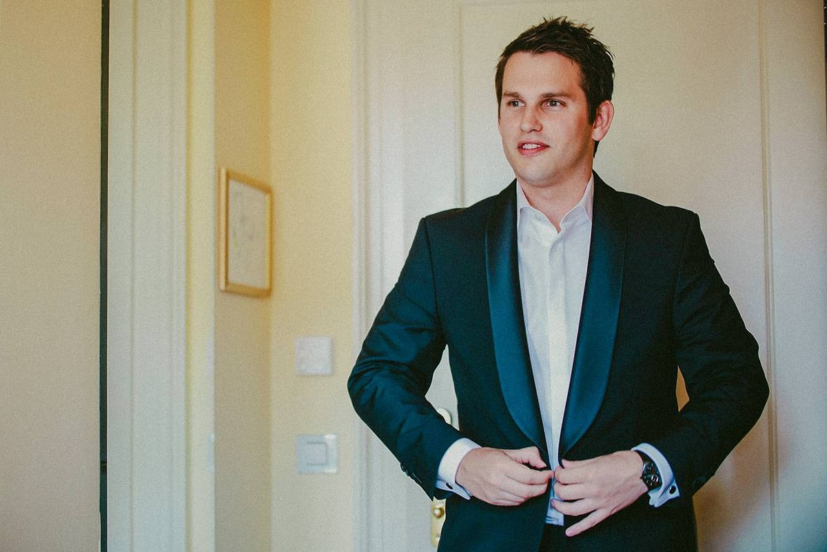 Groom Dan is smiling while putting on his wedding jacket