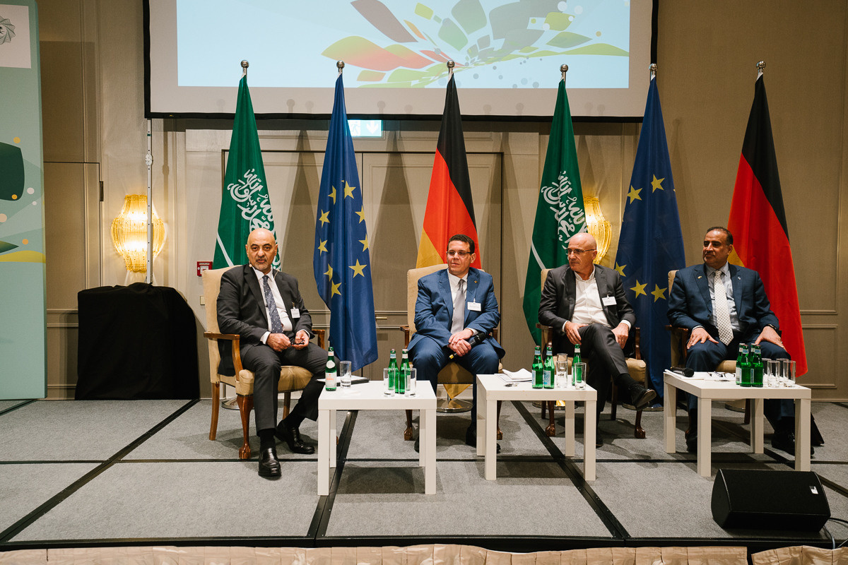 Four speakers sit on stage for a panel discussion with international flags in the background