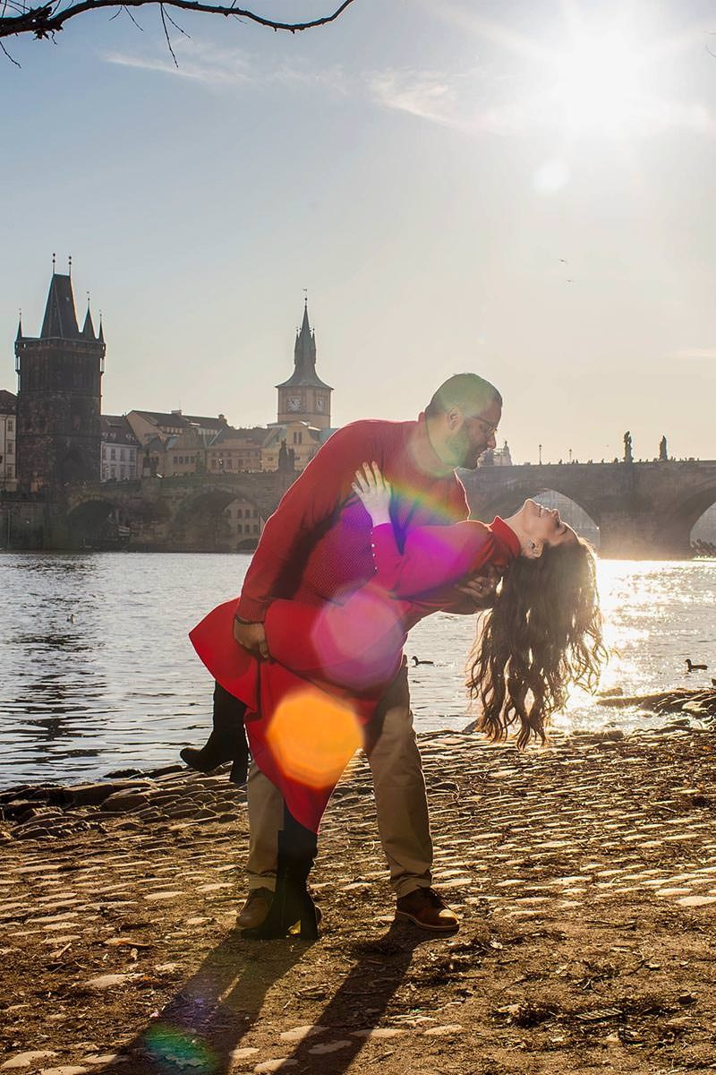 A man dips his partner as the sun flares vividly above them near the riverside in Prague.