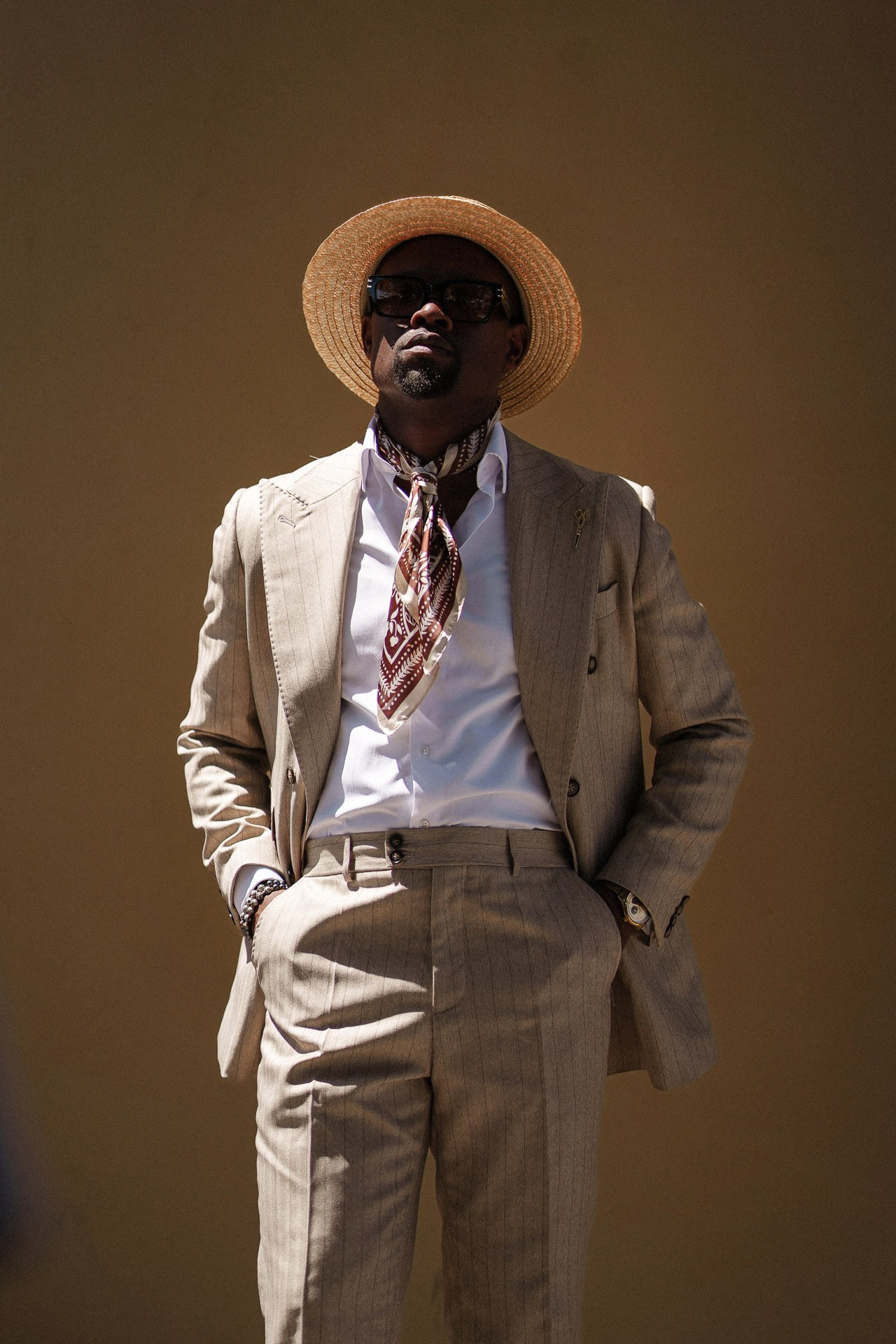 Ritratto da Pitti Uomo 110, ospite in tailoring di lino beige e cappello di paglia in luce calda