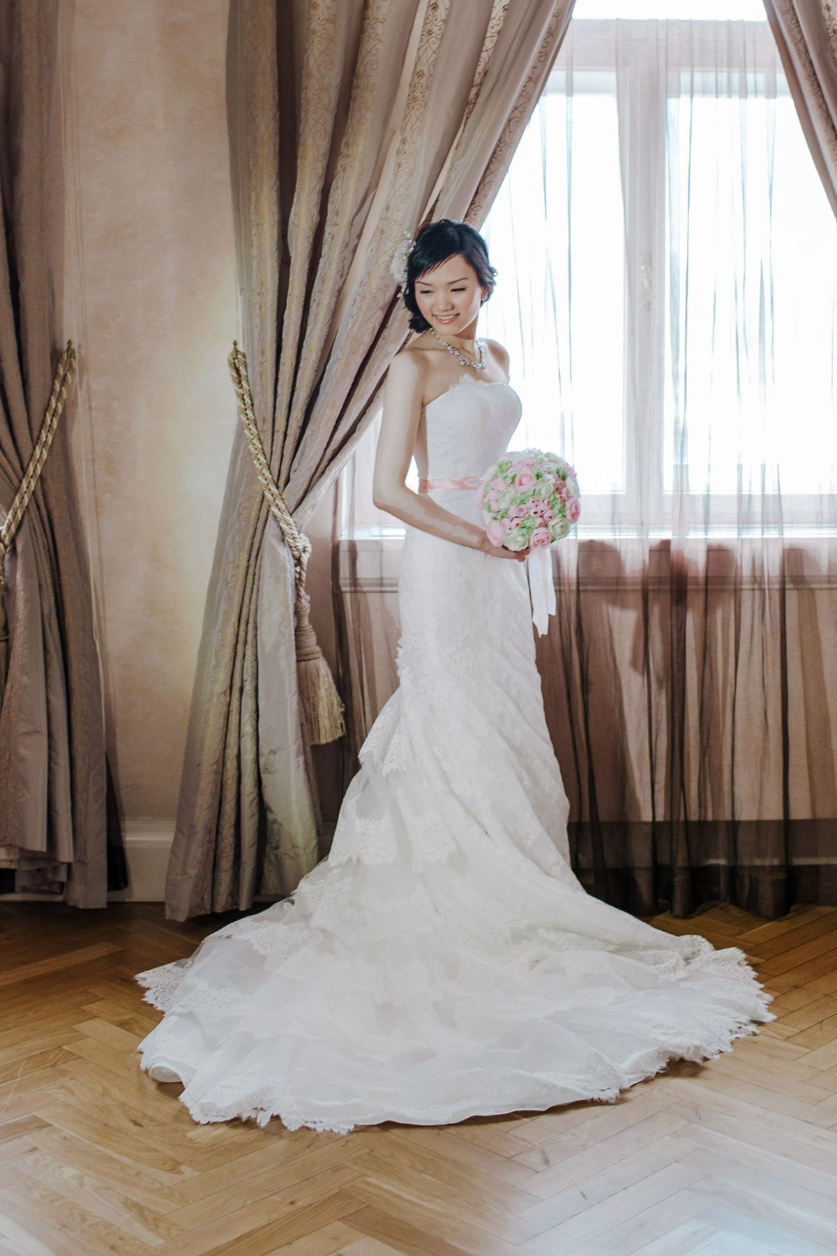 A Hong Kong bride clutching her bouquet poses for an elegant, classical posed photo in her luxury suite in Prague following her bridal preparation.
