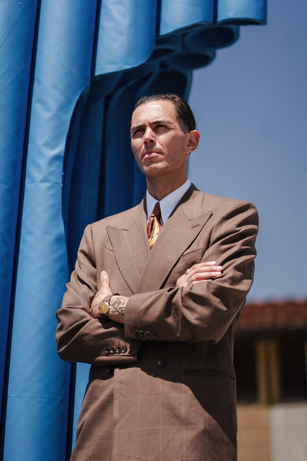 Ritratto street style da Pitti Uomo 110, uomo in completo sartoriale marrone vicino all’installazione blu alla Fortezza da Basso