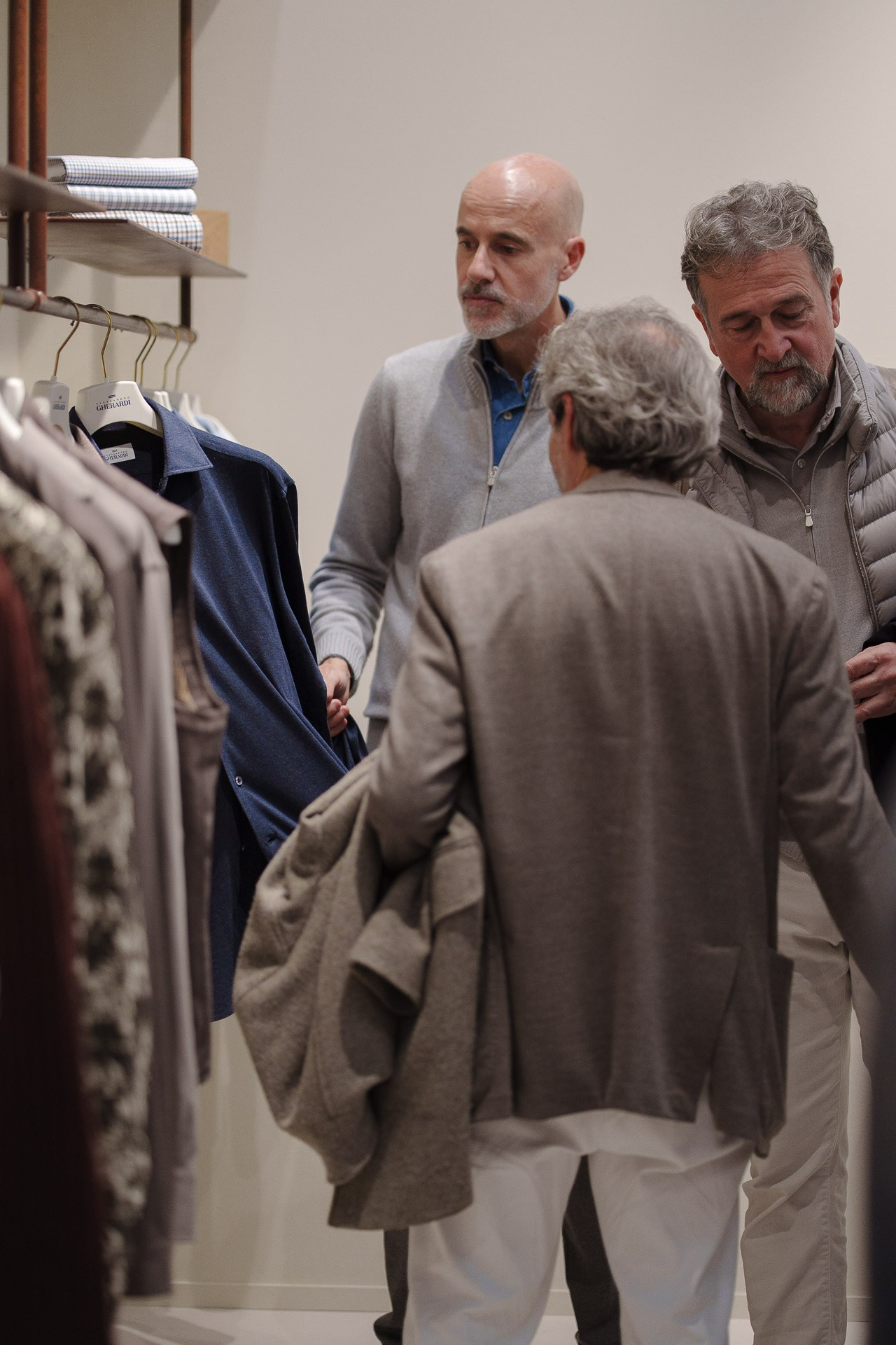 A group of fashion professionals in beige and grey blazers discussing tailoring at a Pitti Uomo 109 booth.