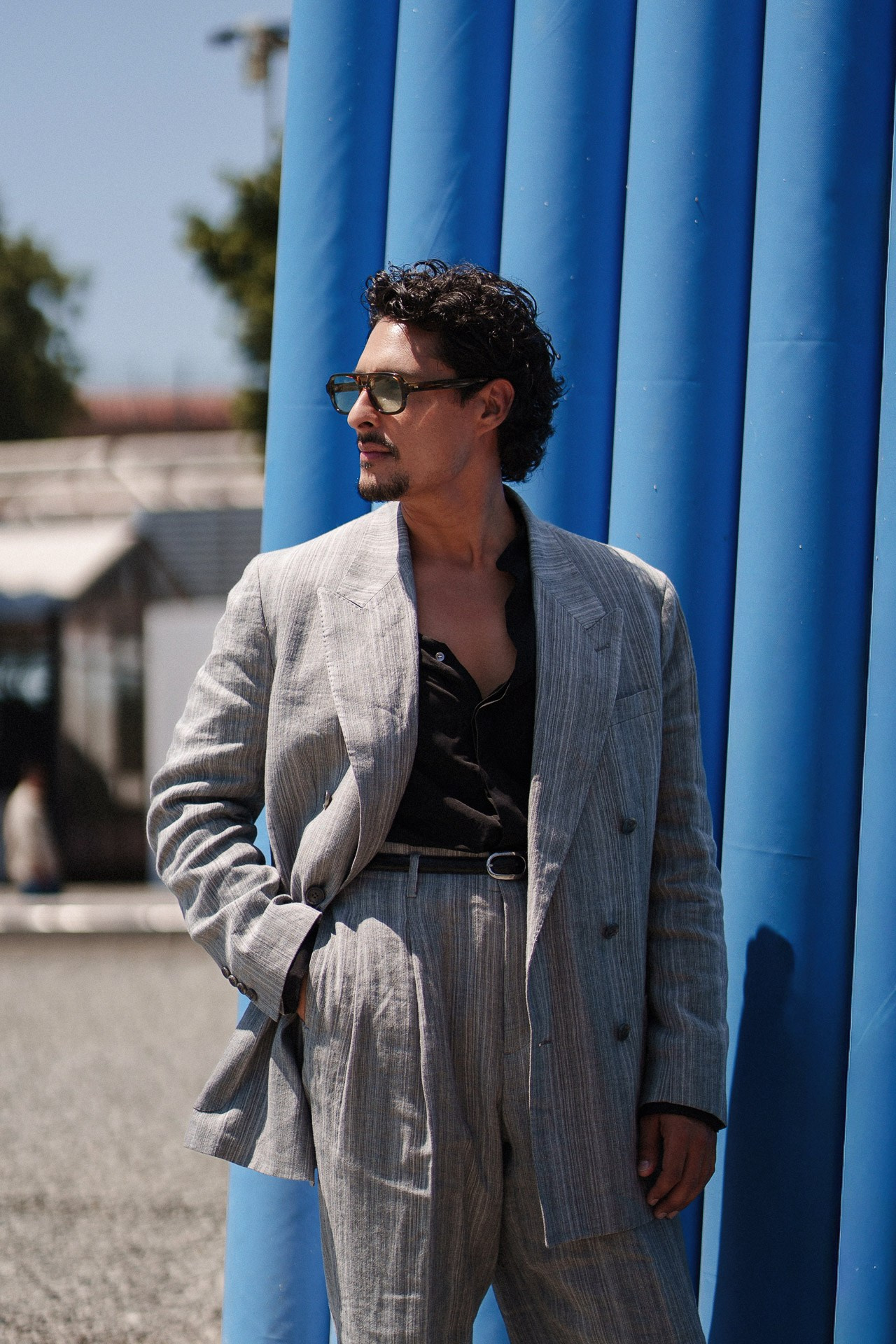 Ritratto street style da Pitti Uomo 110, ospite in completo grigio a righe vicino all’installazione blu alla Fortezza da Basso