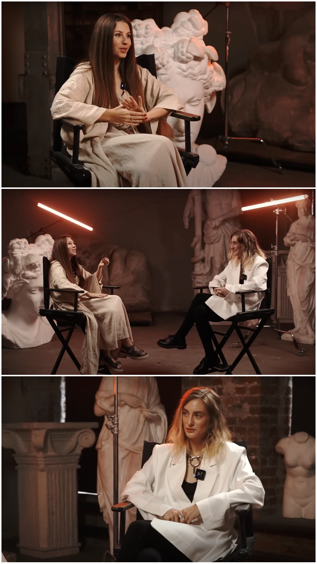 Interview scene with two women in a studio, surrounded by sculptures, one in a white jacket, the other in a beige outfit, seated on black chairs