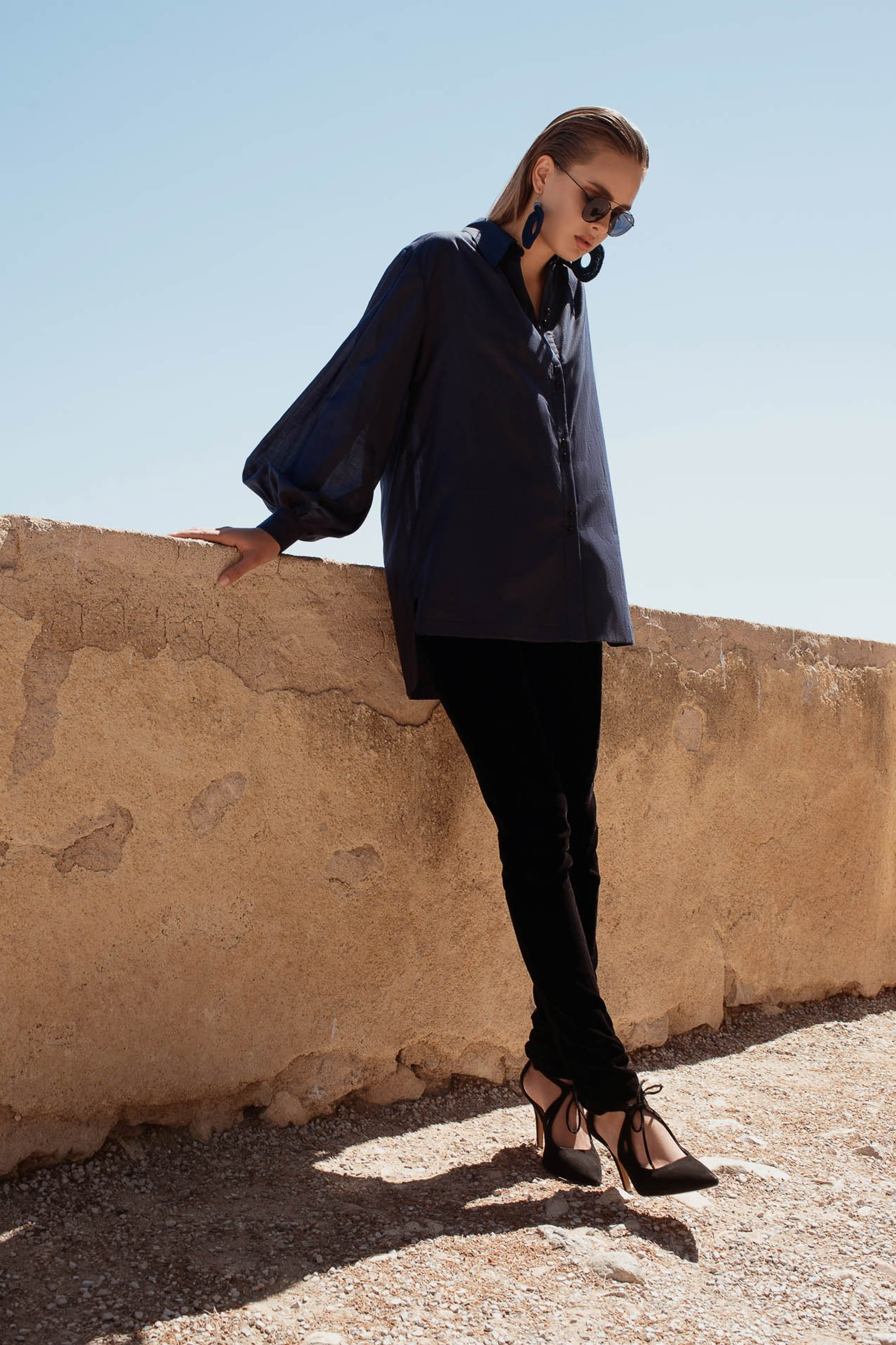 Fashion model in minimalist outfit walking along stone wall, editorial fashion photography