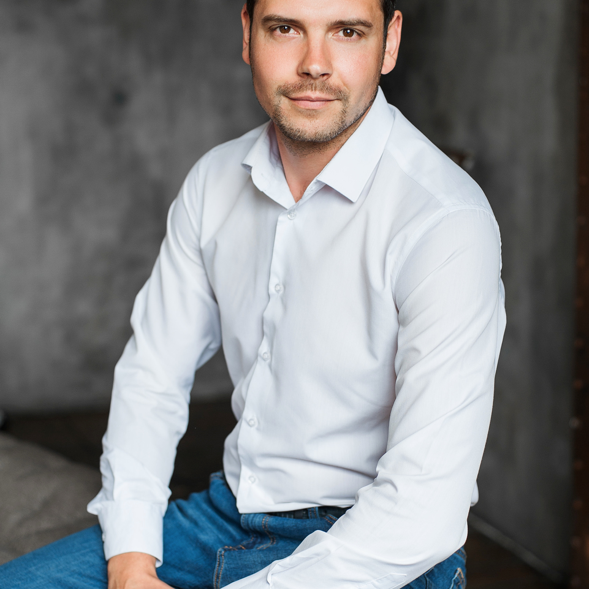 Relaxed business professional in casual attire sitting on a stool for a personal branding portrait by Dmitrii Shmatov