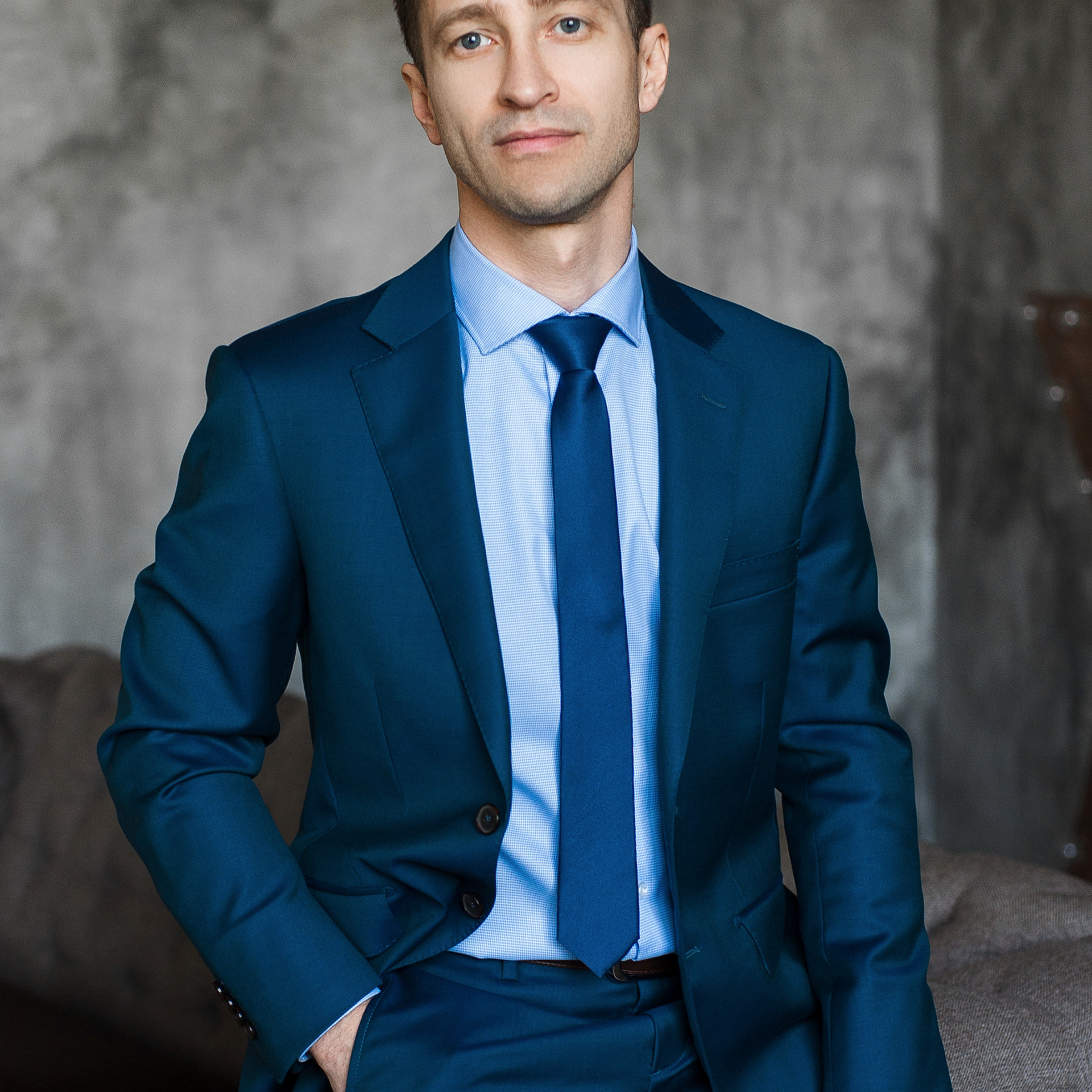 Confident male executive in a blue suit seated comfortably for a professional portrait by Dmitrii Shmatov.