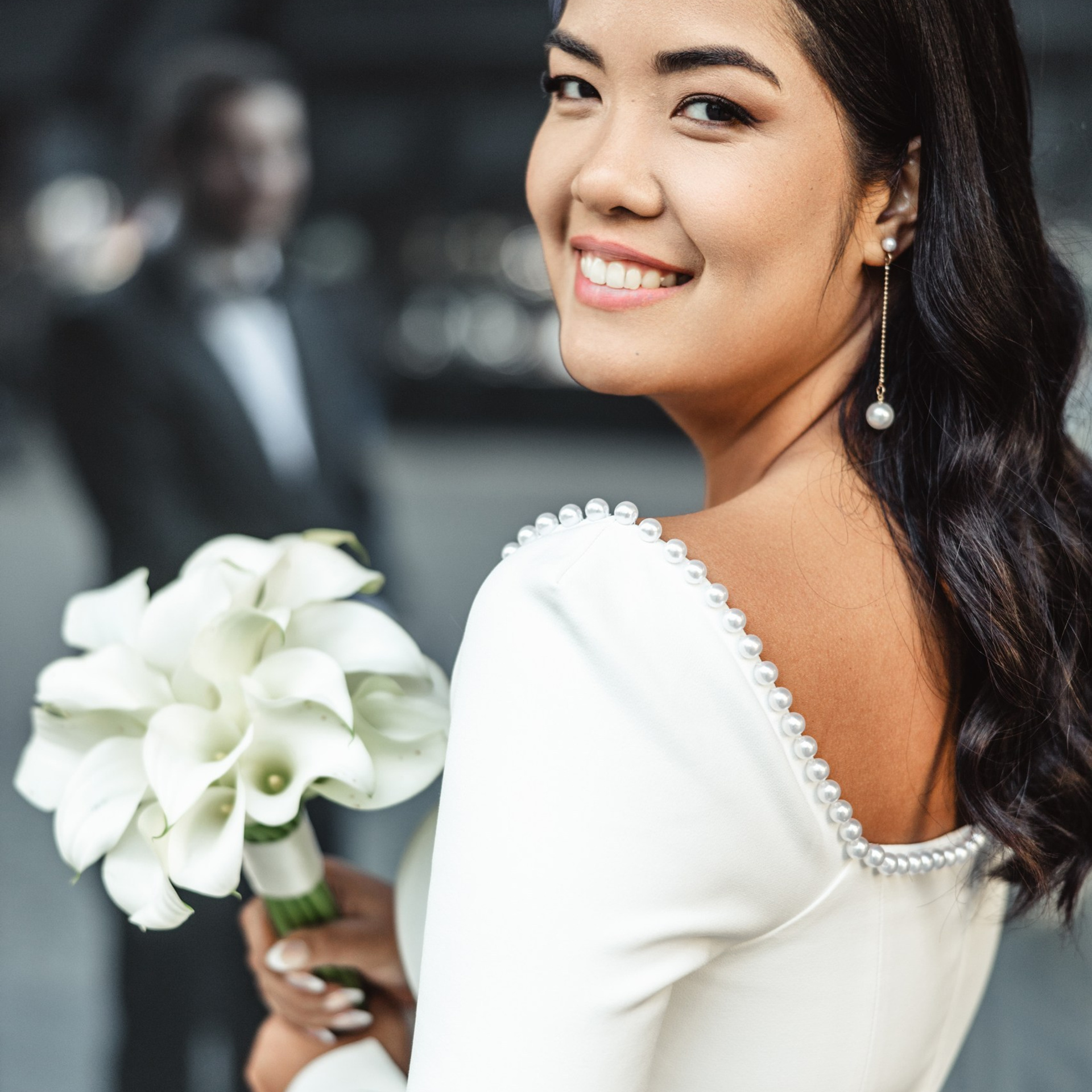 Bruid kijkt glimlachend over haar schouder met haar bruidsboeket in de hand