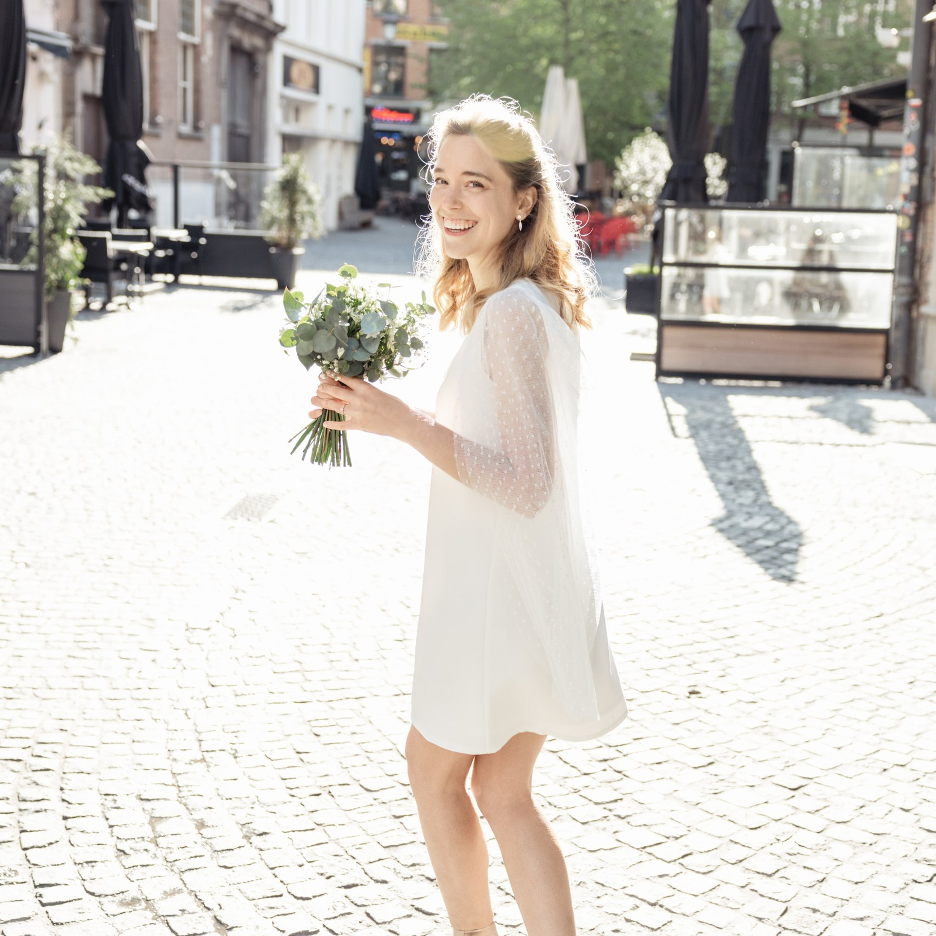 Bruid loopt glimlachend door de straat met een boeket in haar hand