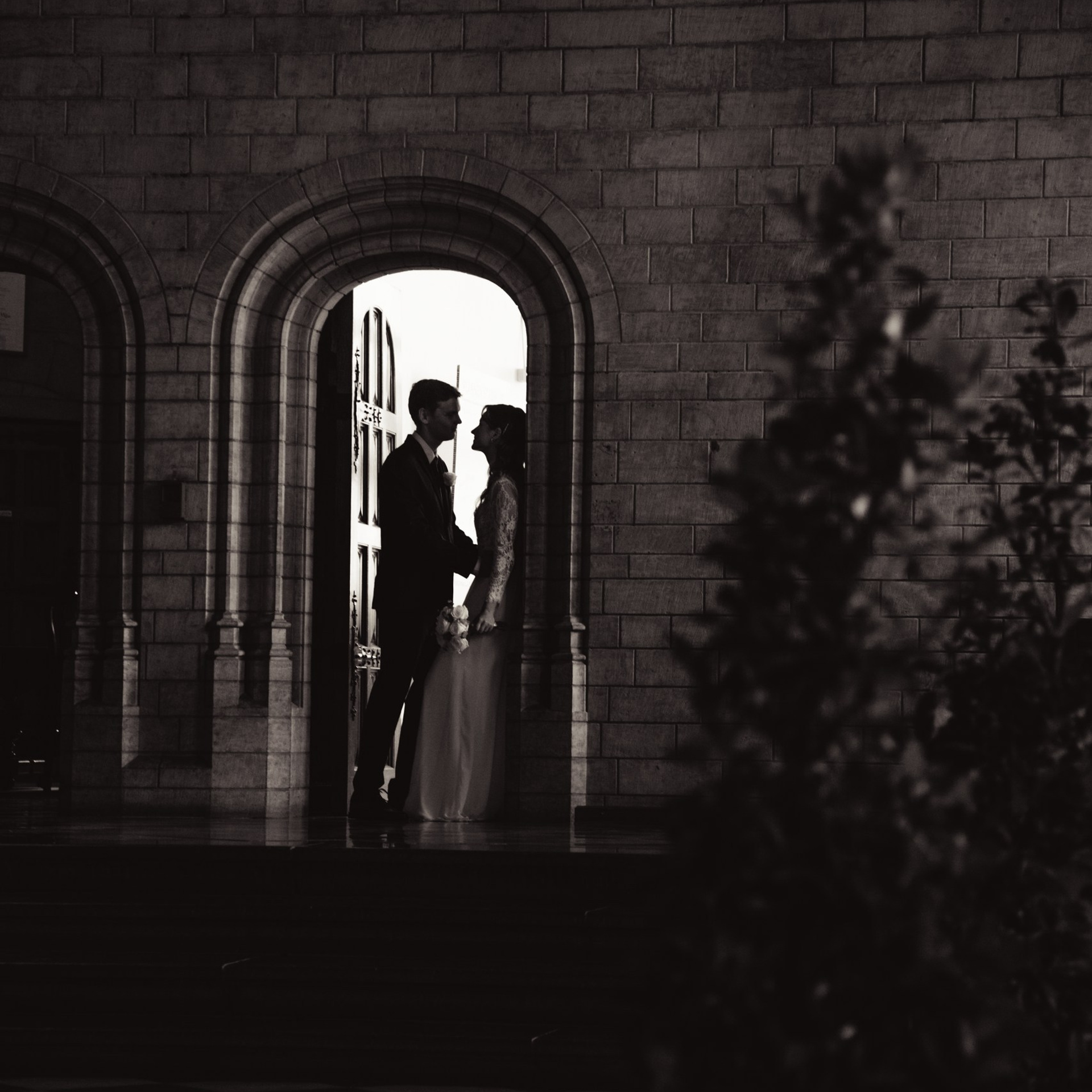 Bruidspaar staat samen in een verlichte deuropening in een donkere setting