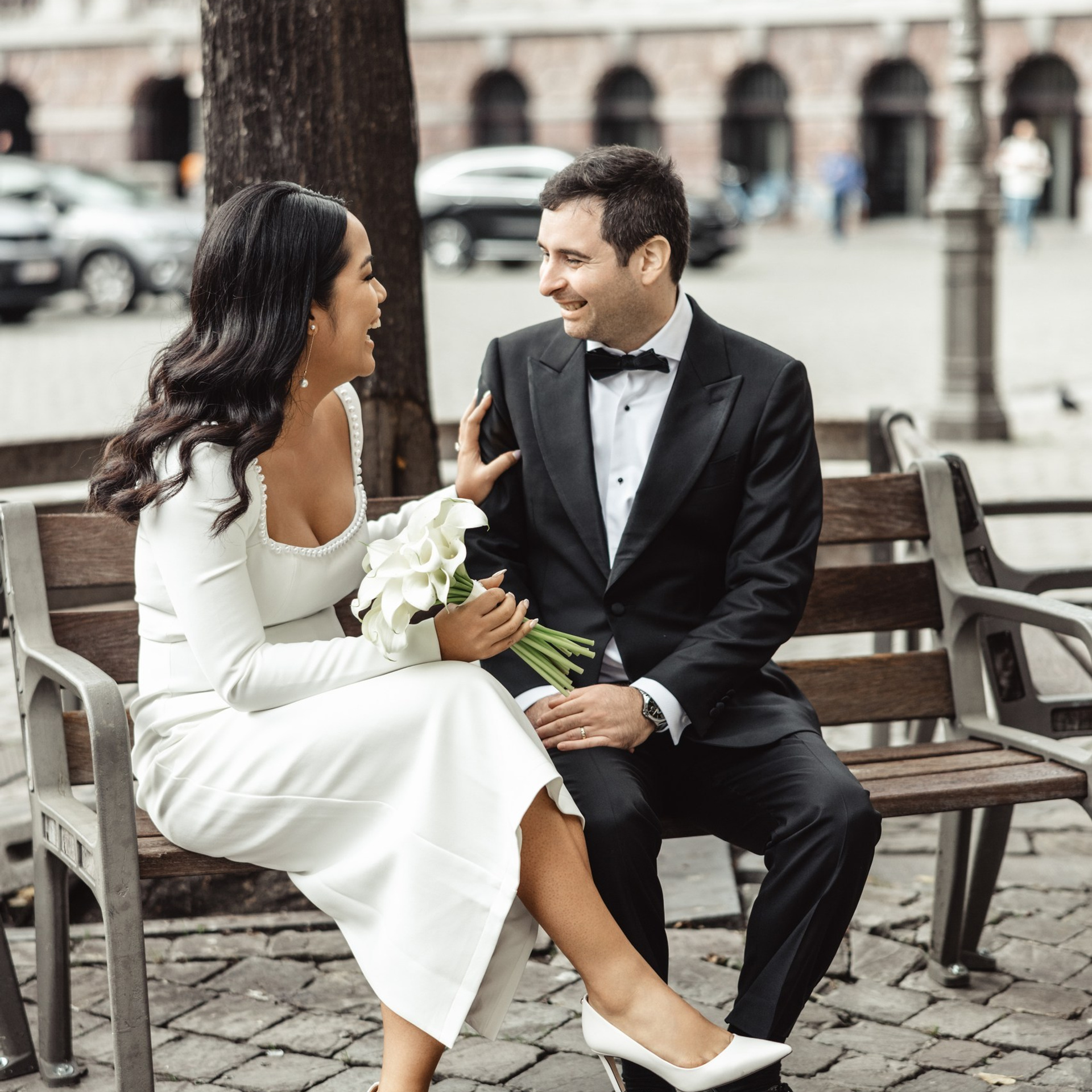 Bruidspaar zit samen op een bankje en kijkt elkaar glimlachend aan