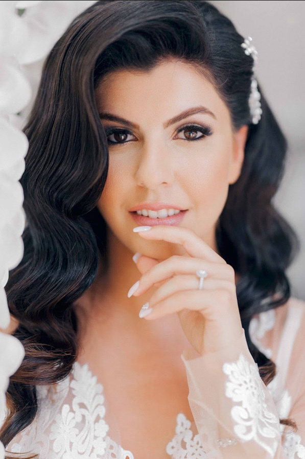 Bride's face with white hair clip on black hair and lace dress.