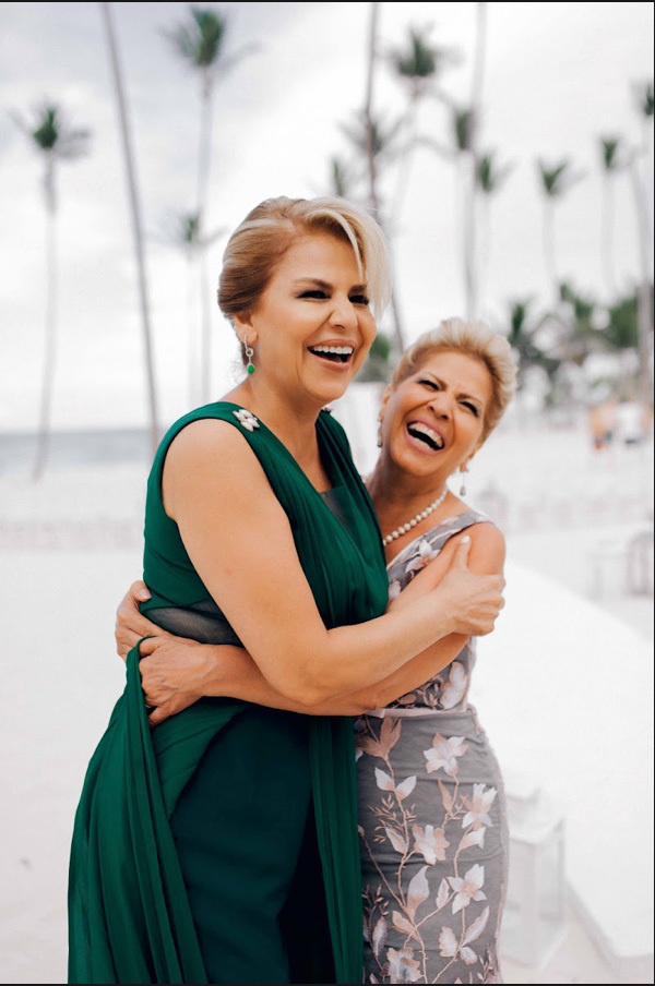Mothers of the bride and groom hug each other on the background of the sea beach with palm trees.
