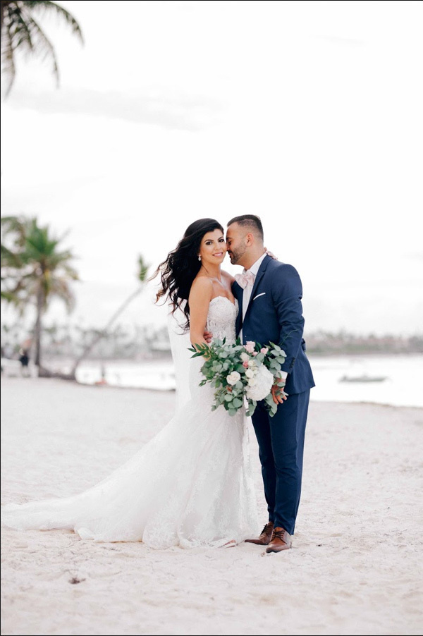 Bride and groom stand embracing on the background of the sea beach with palm trees.