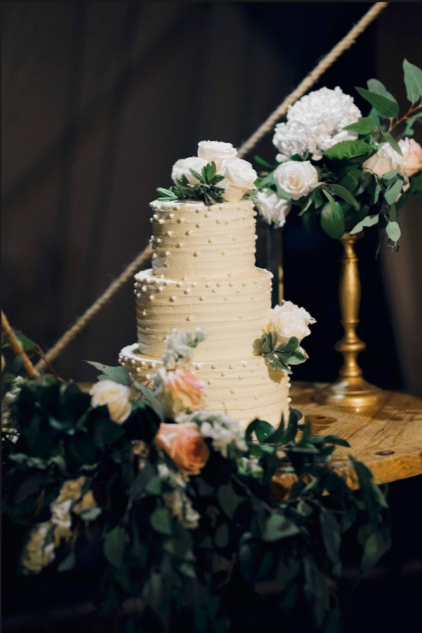 On a dark background, a white wedding cake surrounded by bouquets of white flowers.