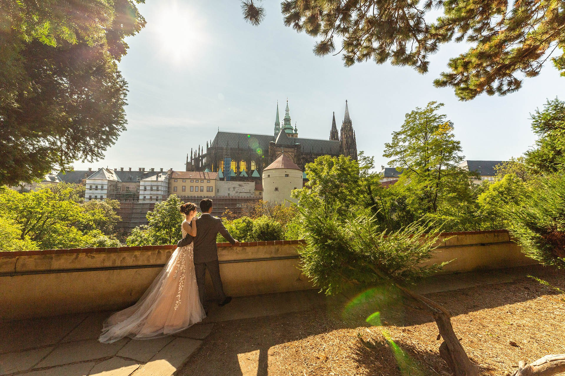 A couple embrace while gazing across the landscape of Prague Castle on a summer day.