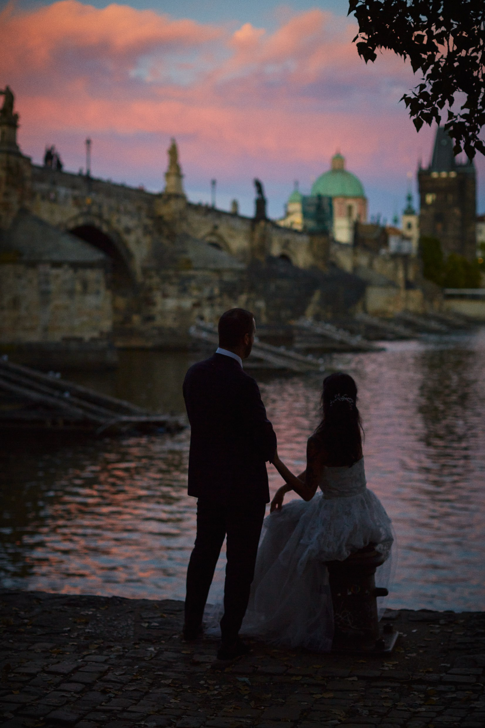Couple silhouette under bridge with colorful sky.