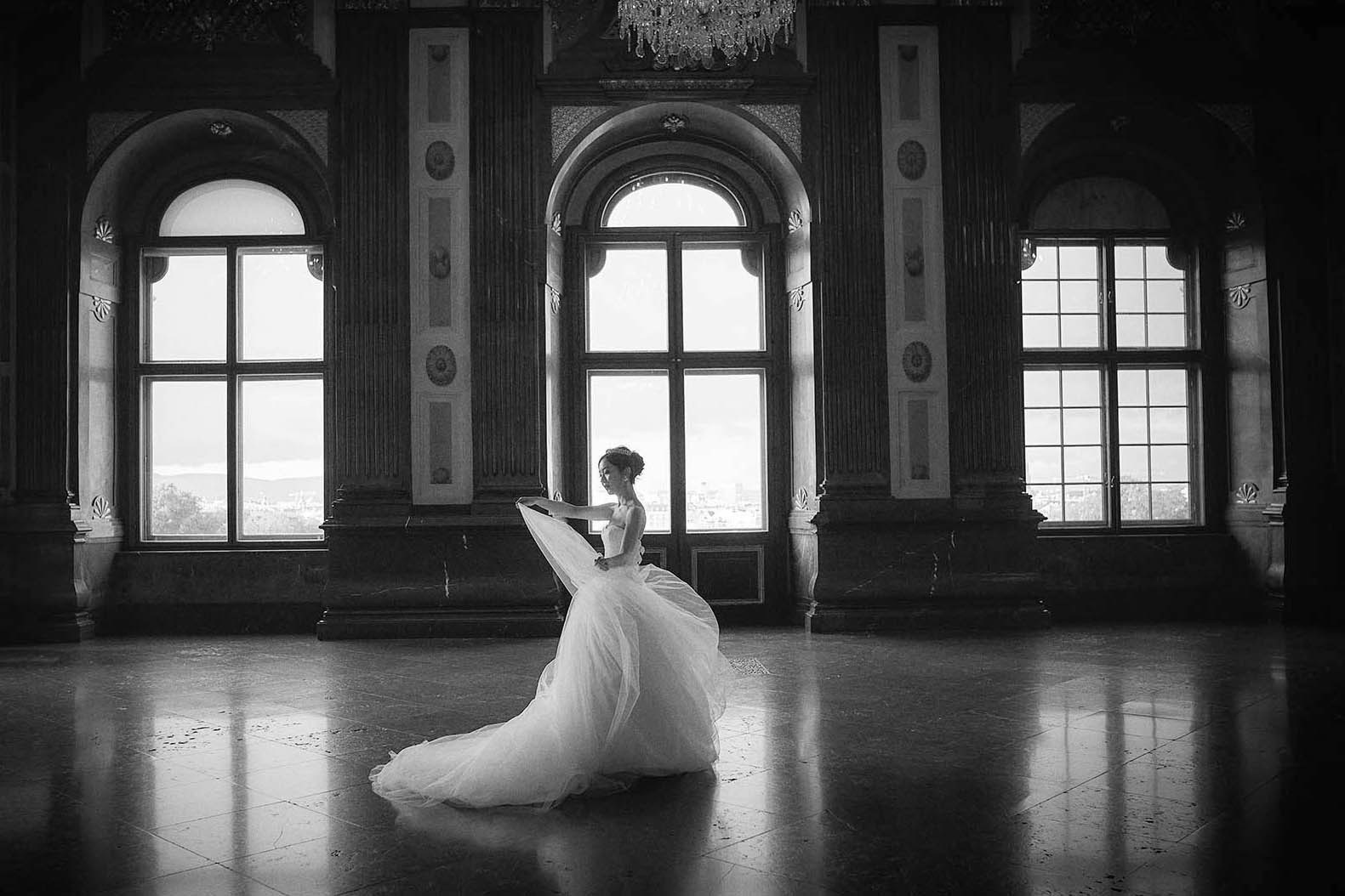 The bride with a flowing dress walks through the Belvedere Palace in Vienna.