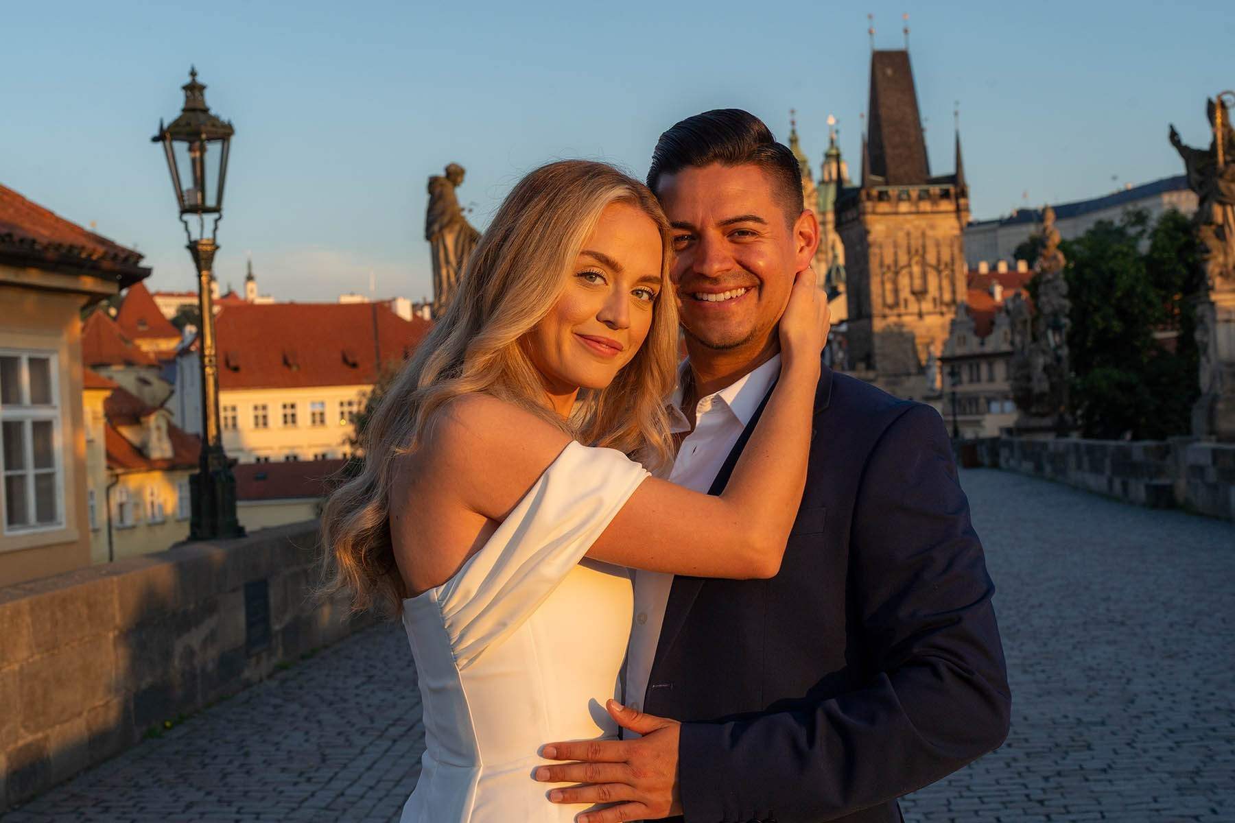 An attractive couple looks into the camera's gaze during their sunrise engagement on the Charles Bridge.