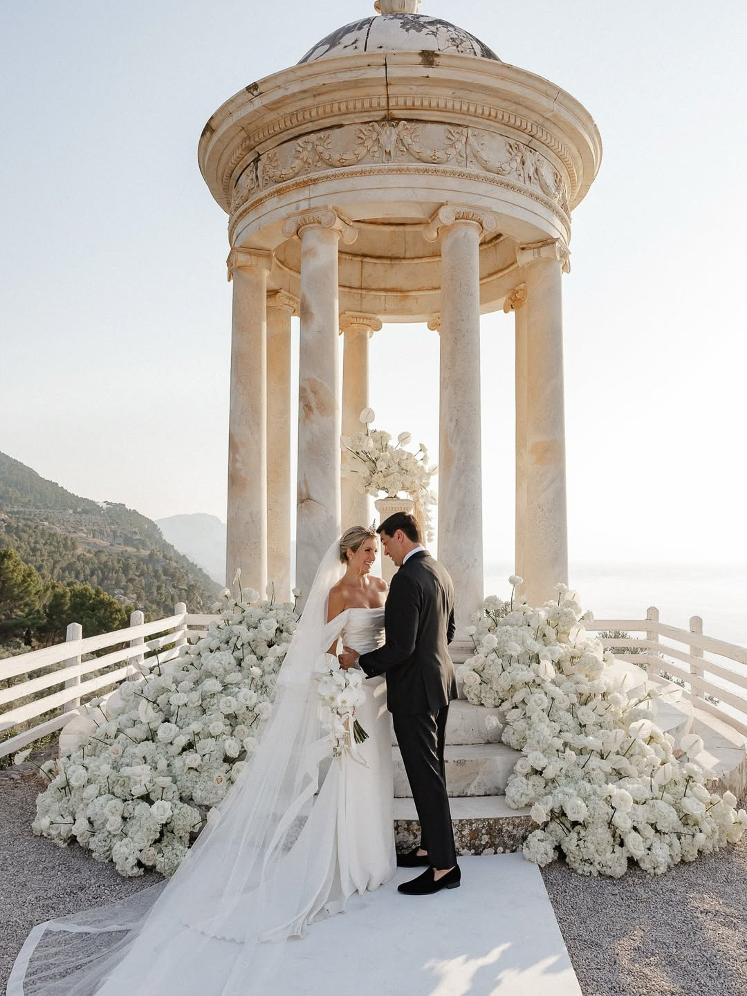 Bride and groom embracing at the Son Marroig temple surrounded by white floral arrangements