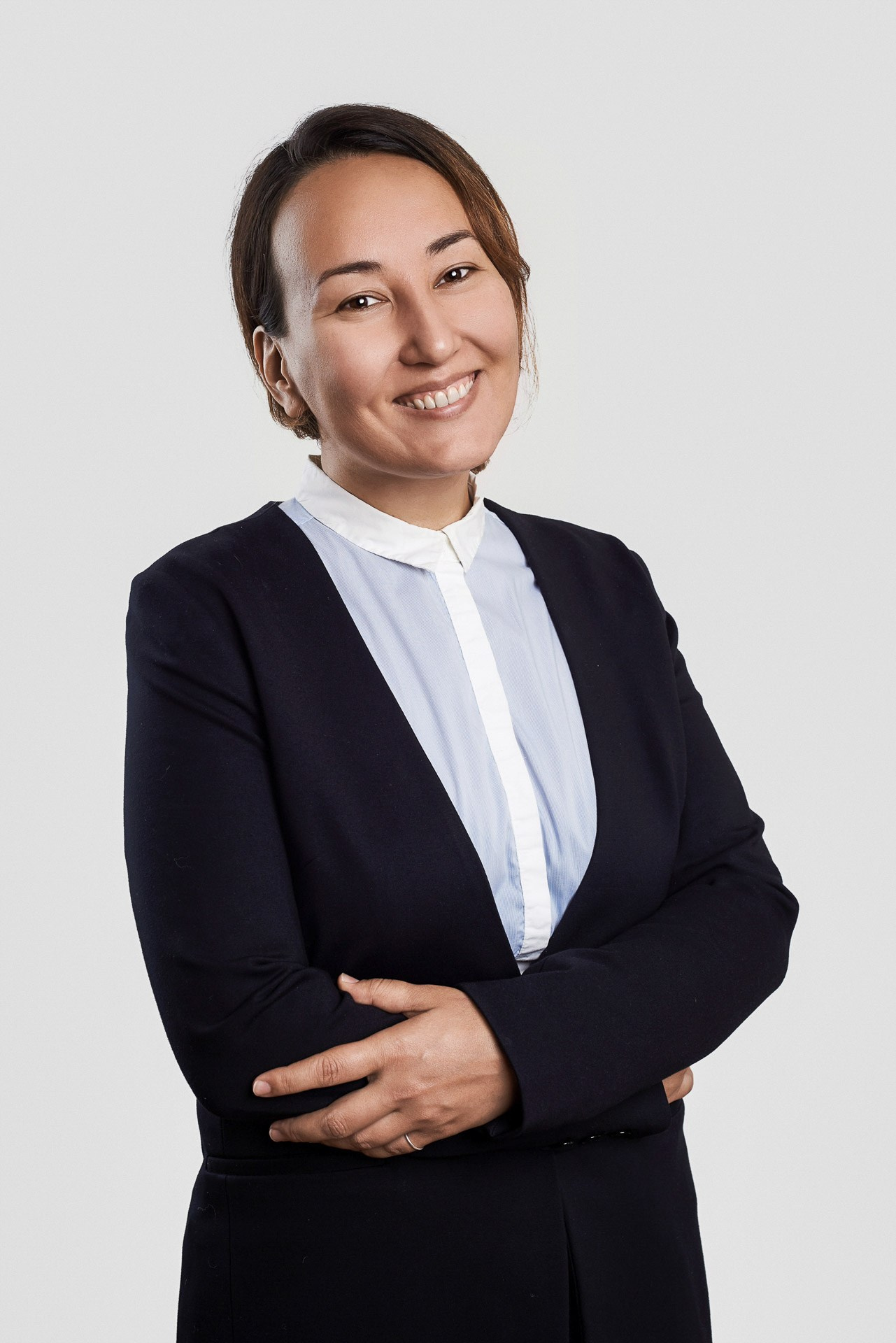Friendly team member portrait for a corporate website, woman in a black jacket and blue shirt on a light background.