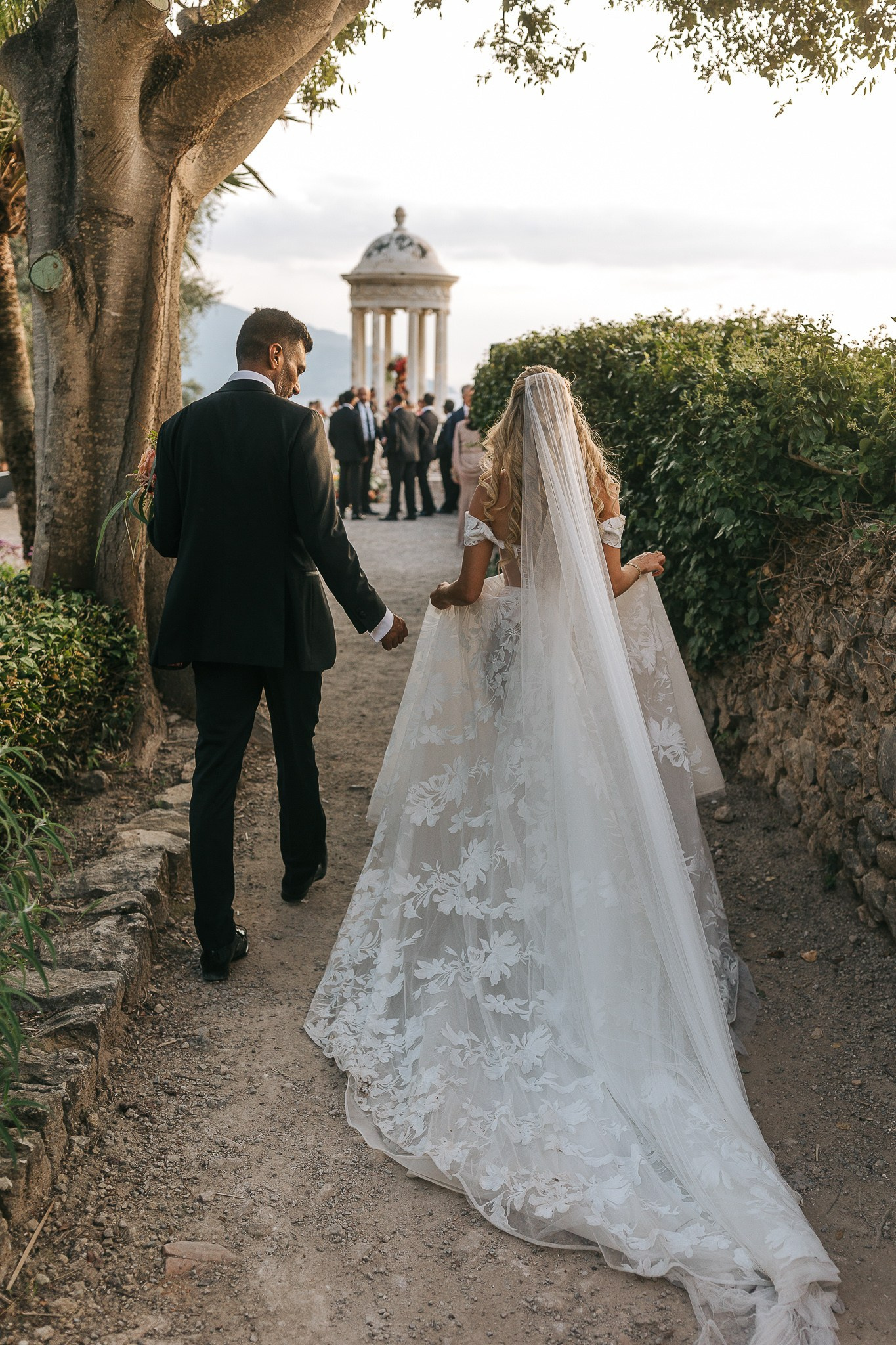 Bride and groom walking hand in hand toward the Son Marroig temple before their wedding ceremony