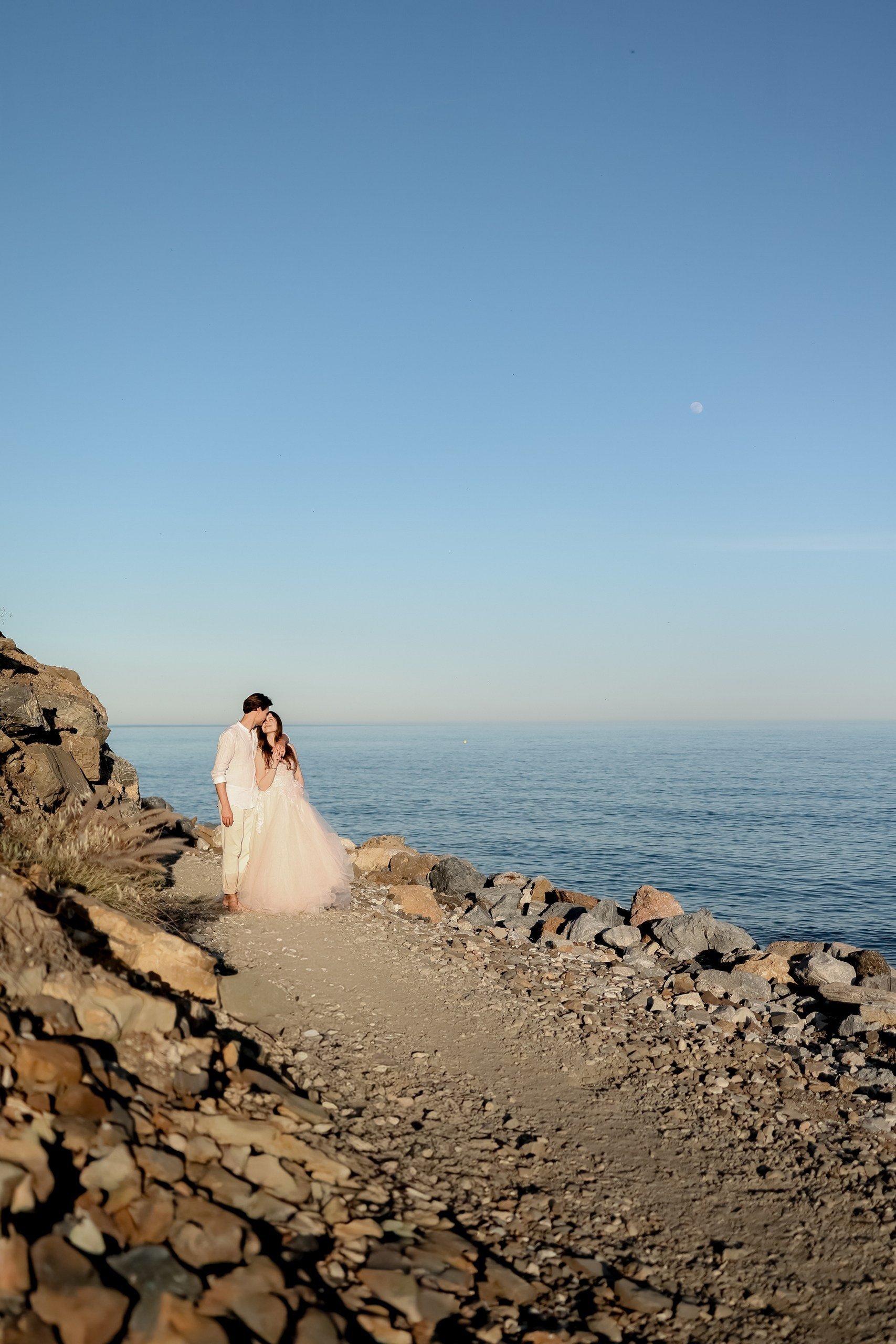 Bräutigam küsst zart dieBraut, sie lächelt glücklich, Meer im Hintergrund, After Wedding Shooting Spanien