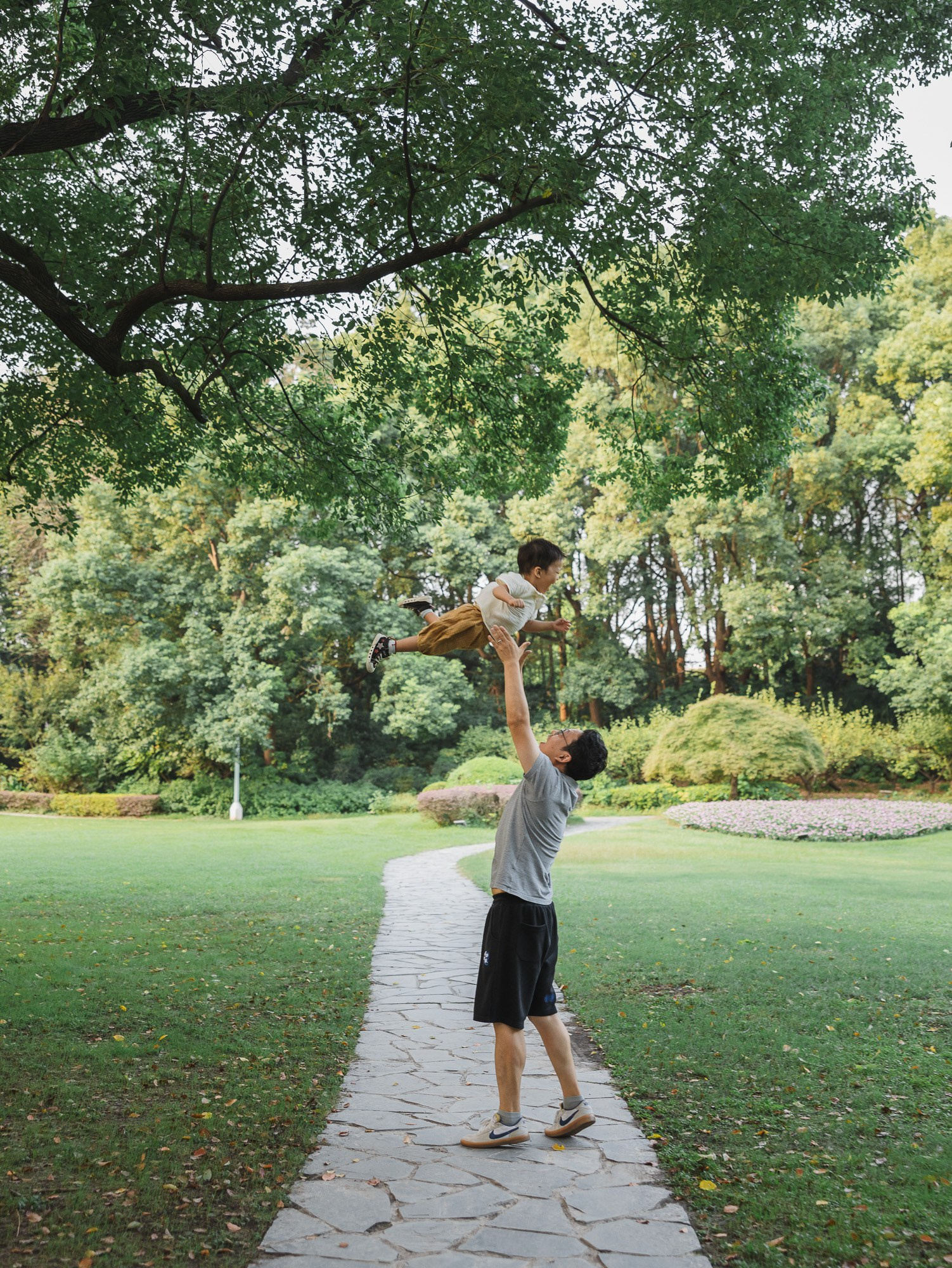 Dad lifts his child high in the air while mom watches nearby during a playful family photography session.
