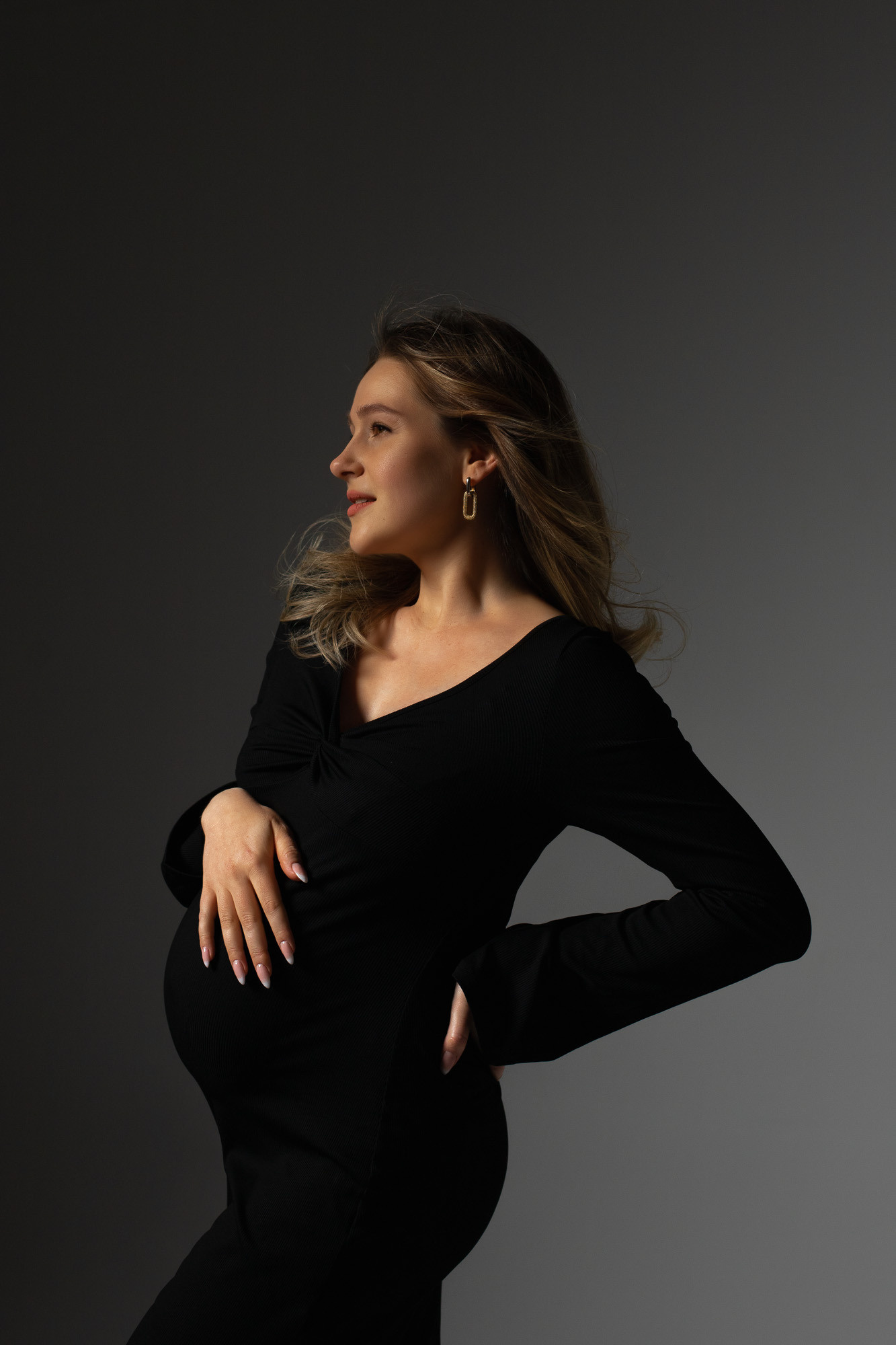 Schwangerschaft Bilder im Studio mit junger Frau in schwarzem Kleid