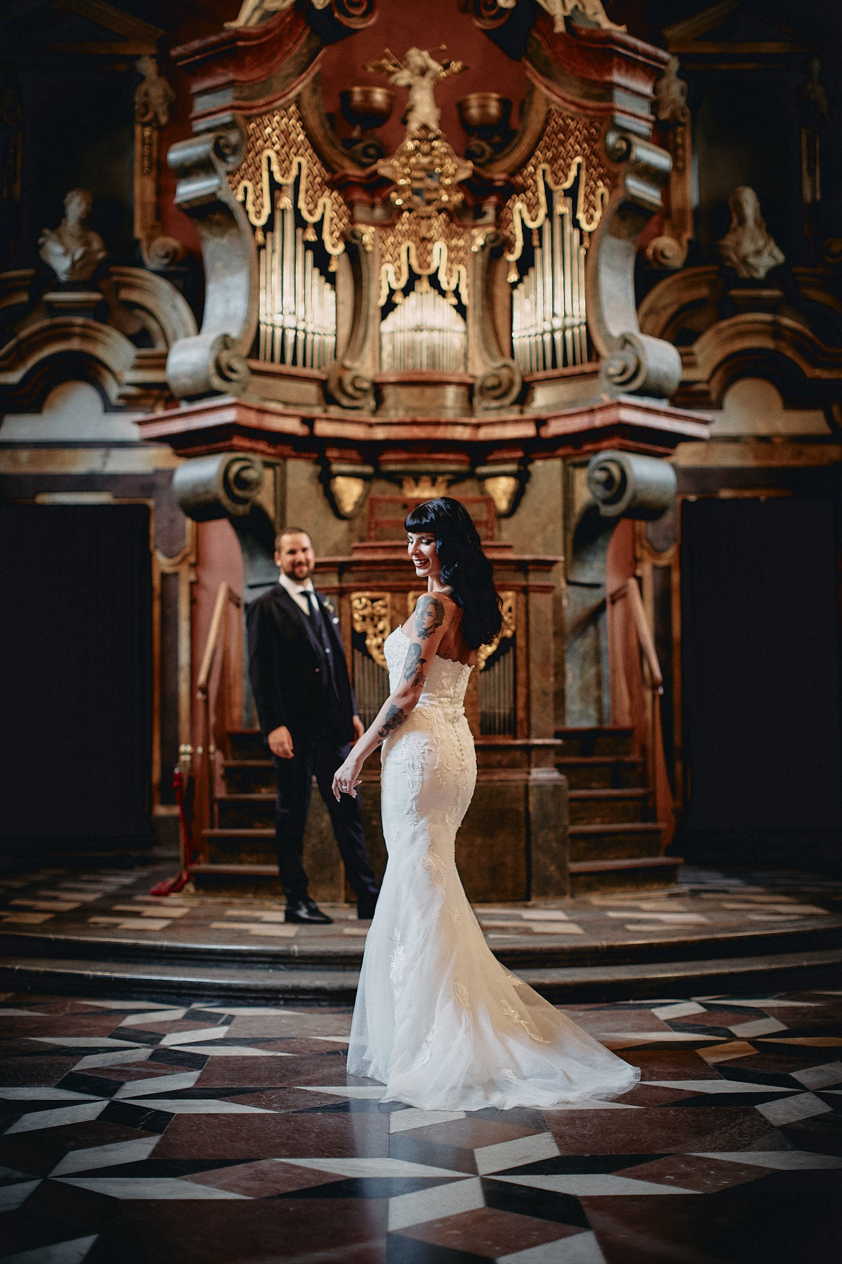 Tattooed bride confident pose with admiring groom at chapel altar.