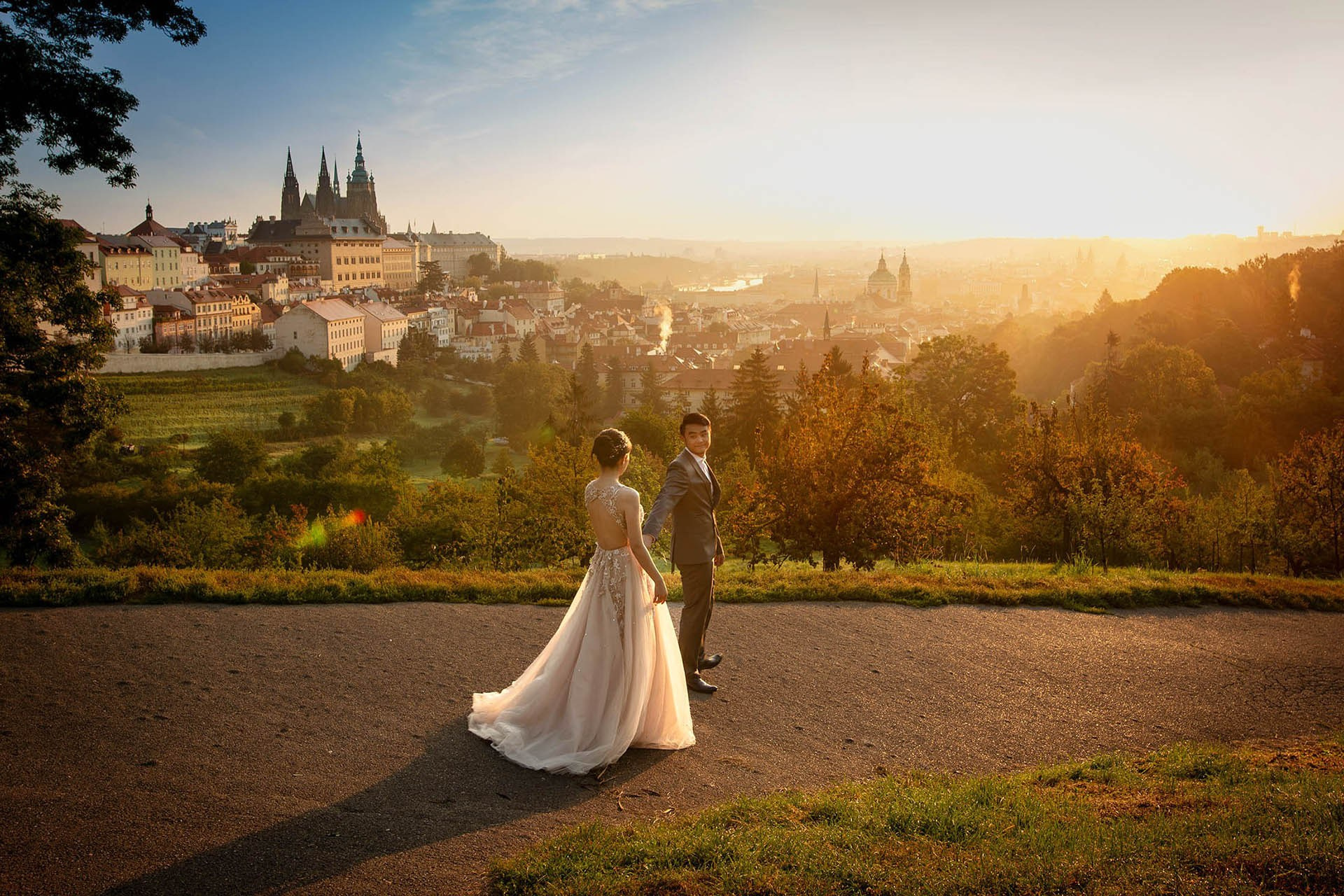 A couple strolls above the urban landscape of Prague near the vineyards of Prague Castle at sunrise.
