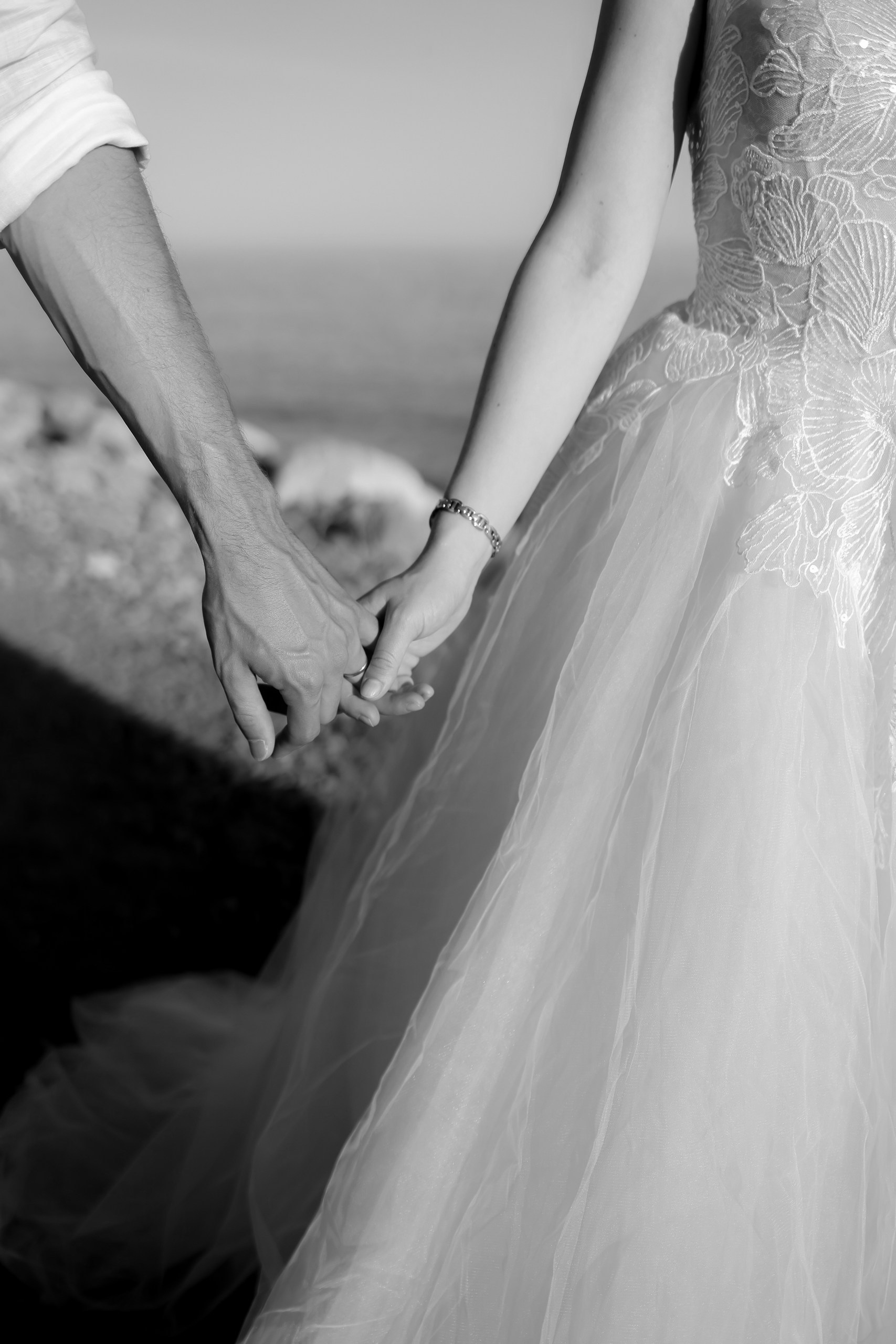 Schwarzweiß Detailaufnahme: Hände des Brautpaares halten sich, Brautkleid-Spitze sichtbar, Hochzeitsfotografin Costa Blanca