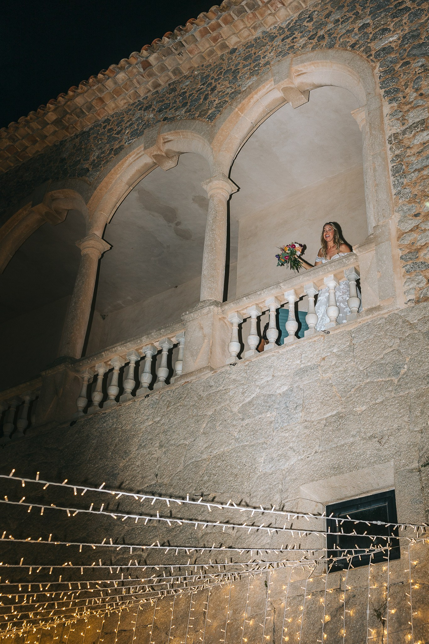 Bride laughing on a stone balcony holding her bouquet at her Mallorca wedding venue