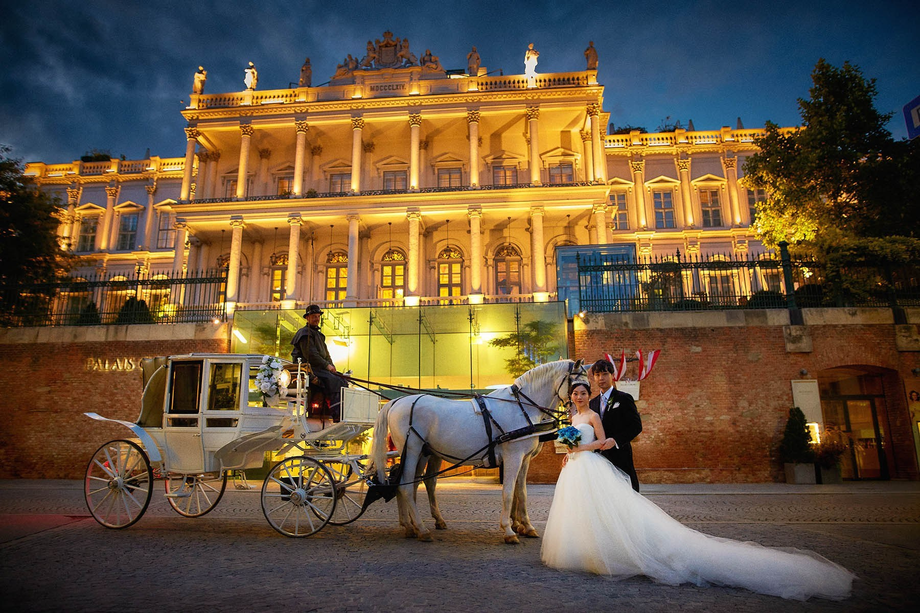 Newlyweds with horse carriage front of illuminated Palais Coburg.