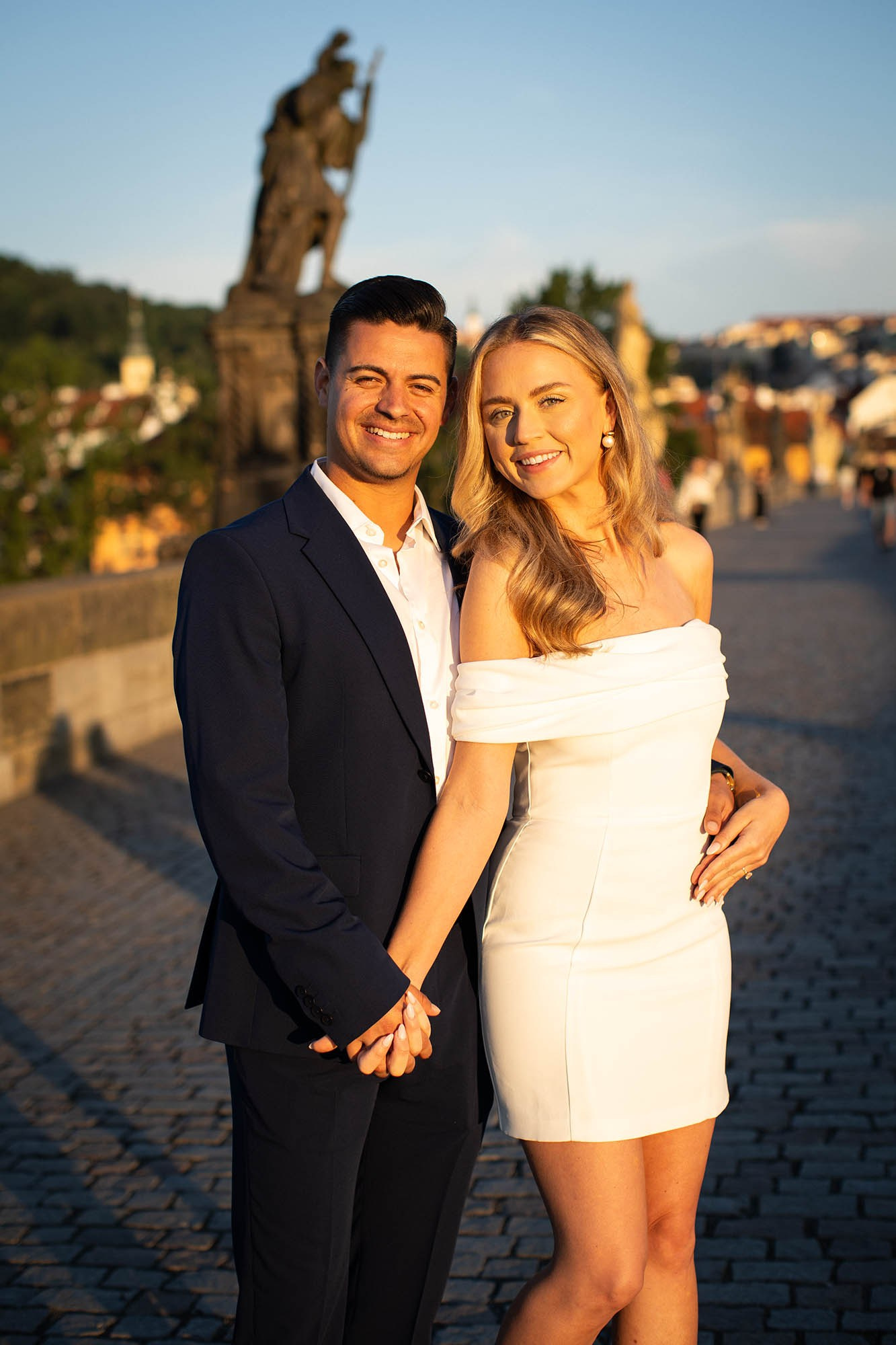 The blonde-haired woman and her stylish partner are bathed in the early morning Golden Light as statues fill their background.