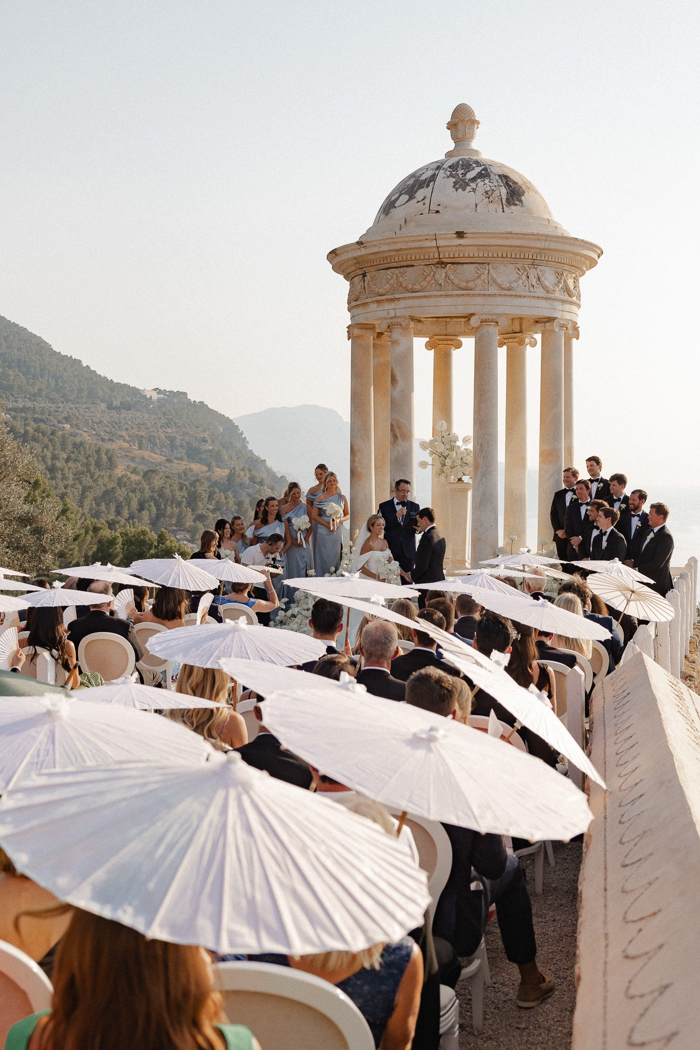 Guests holding white parasols during an outdoor wedding ceremony at Son Marroig, Mallorca