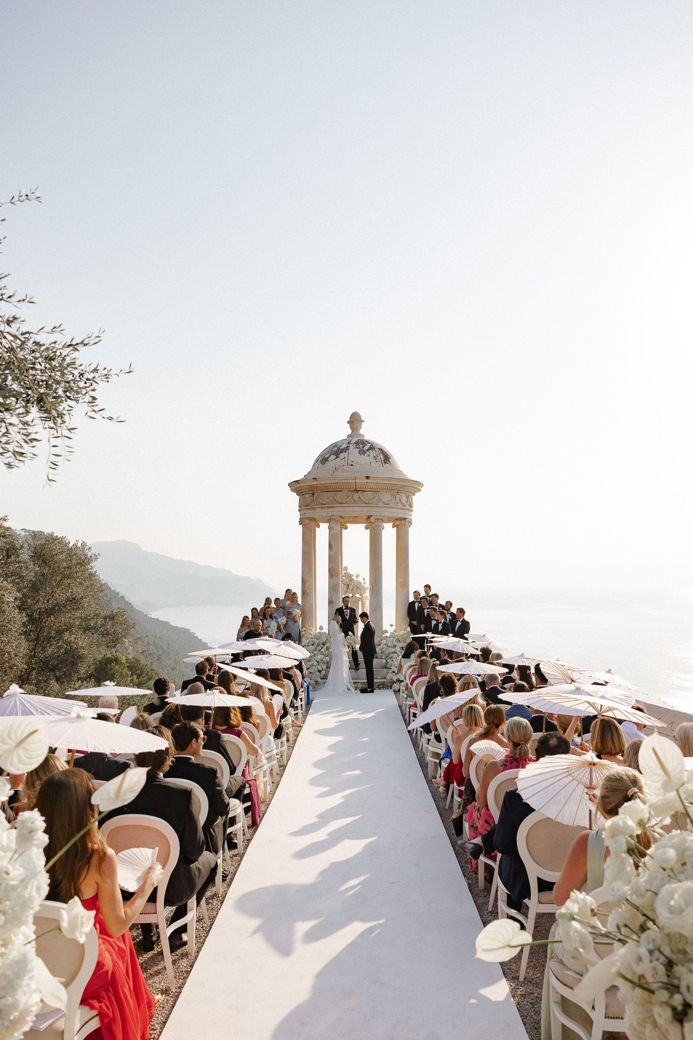Wide view of the wedding ceremony at Son Marroig with guests holding white parasols