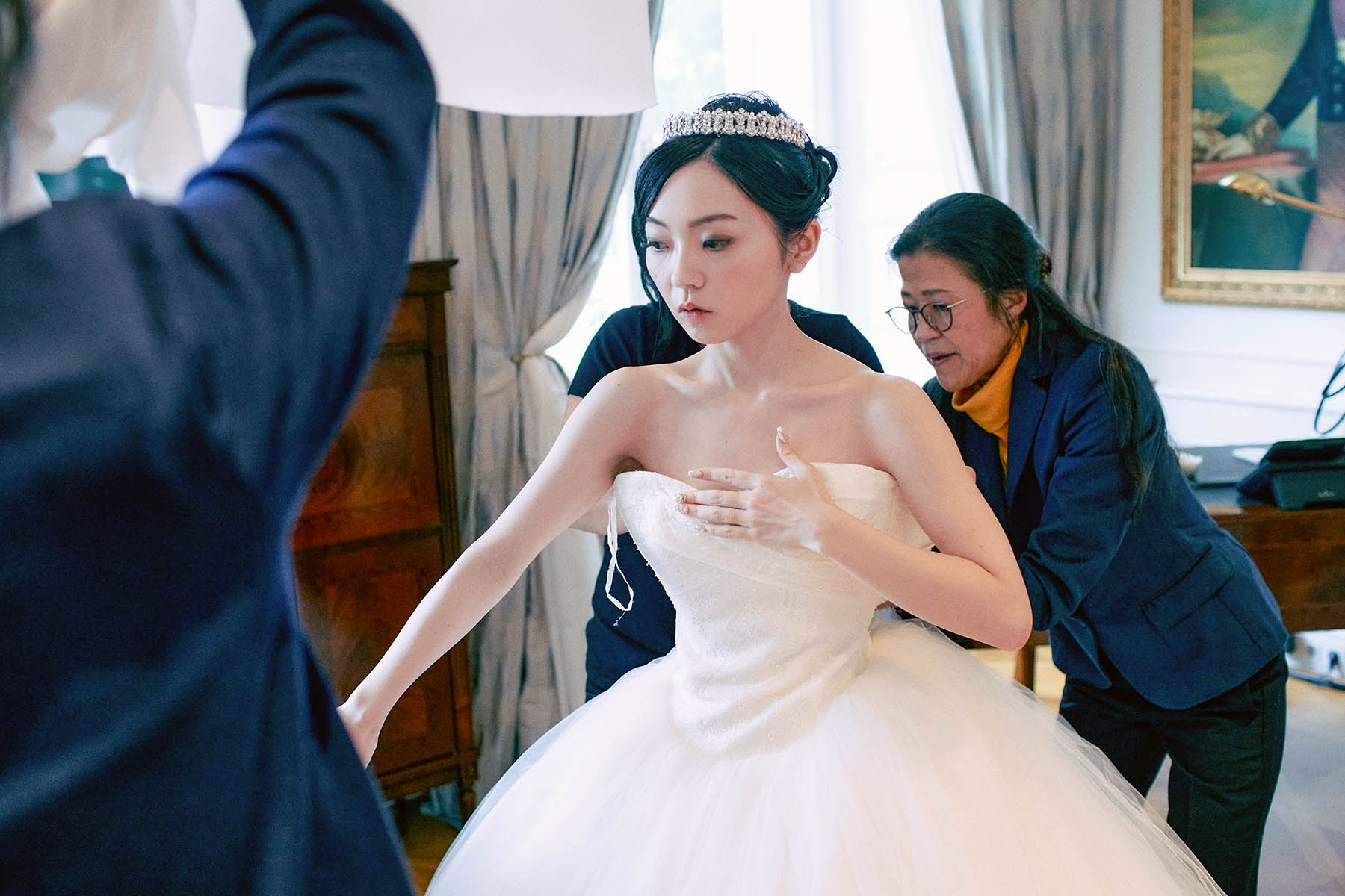 Bride being dressed in wedding gown with assistants at Palais Coburg.